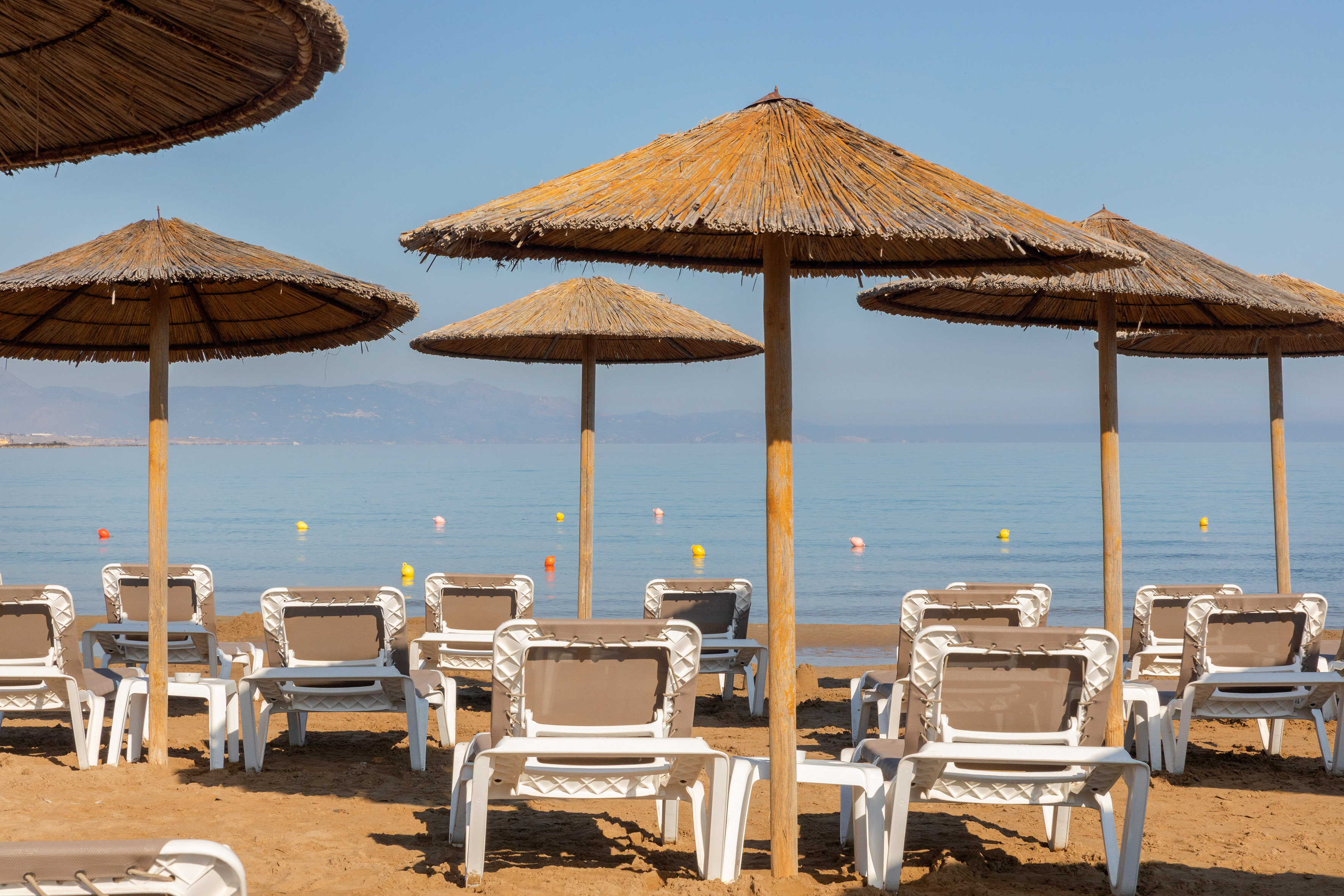 Sandy beach with straw umbrellas, white sun loungers, and calm blue sea.