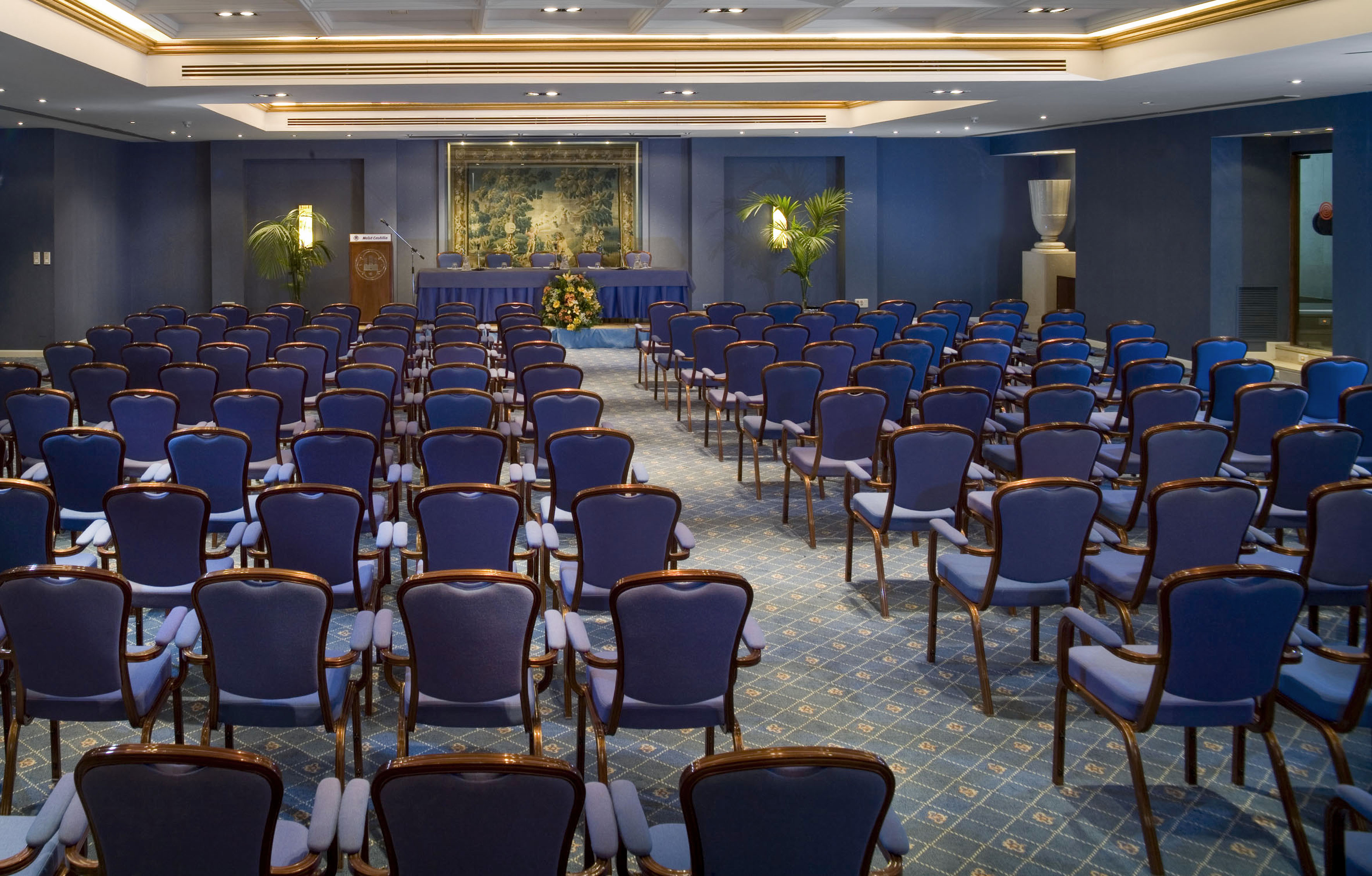 Empty blue conference room with rows of chairs and a presentation stage.