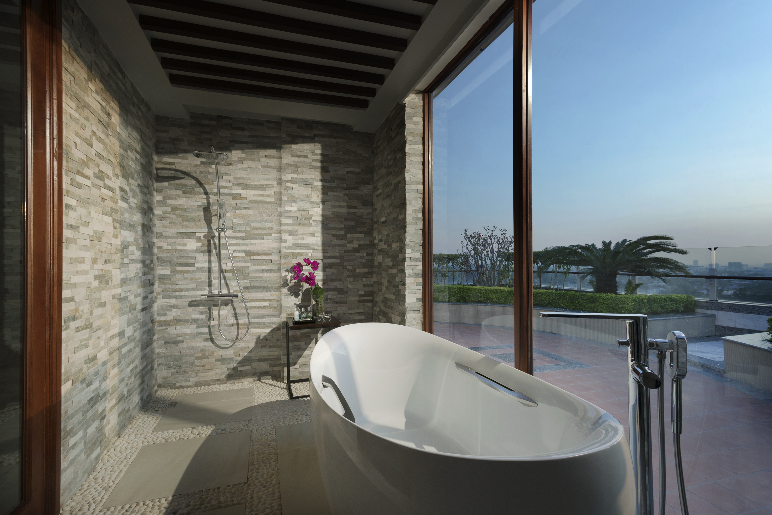 Luxury bathroom with modern tub, stone shower, and scenic city view.