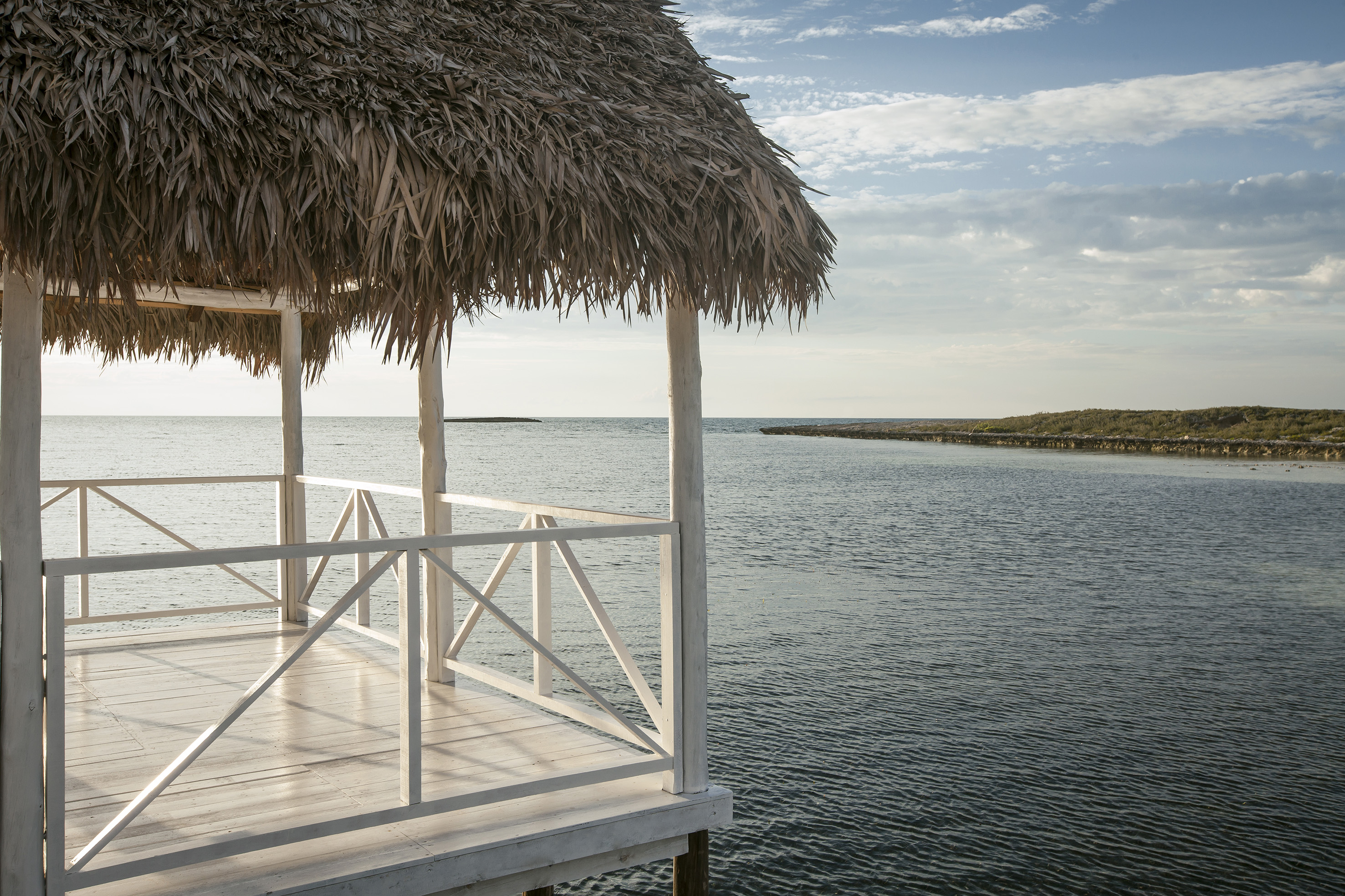 a white wooden structure with a straw roof over water