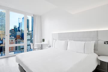 a white bed with white sheets and a table and chairs in a room with a city view