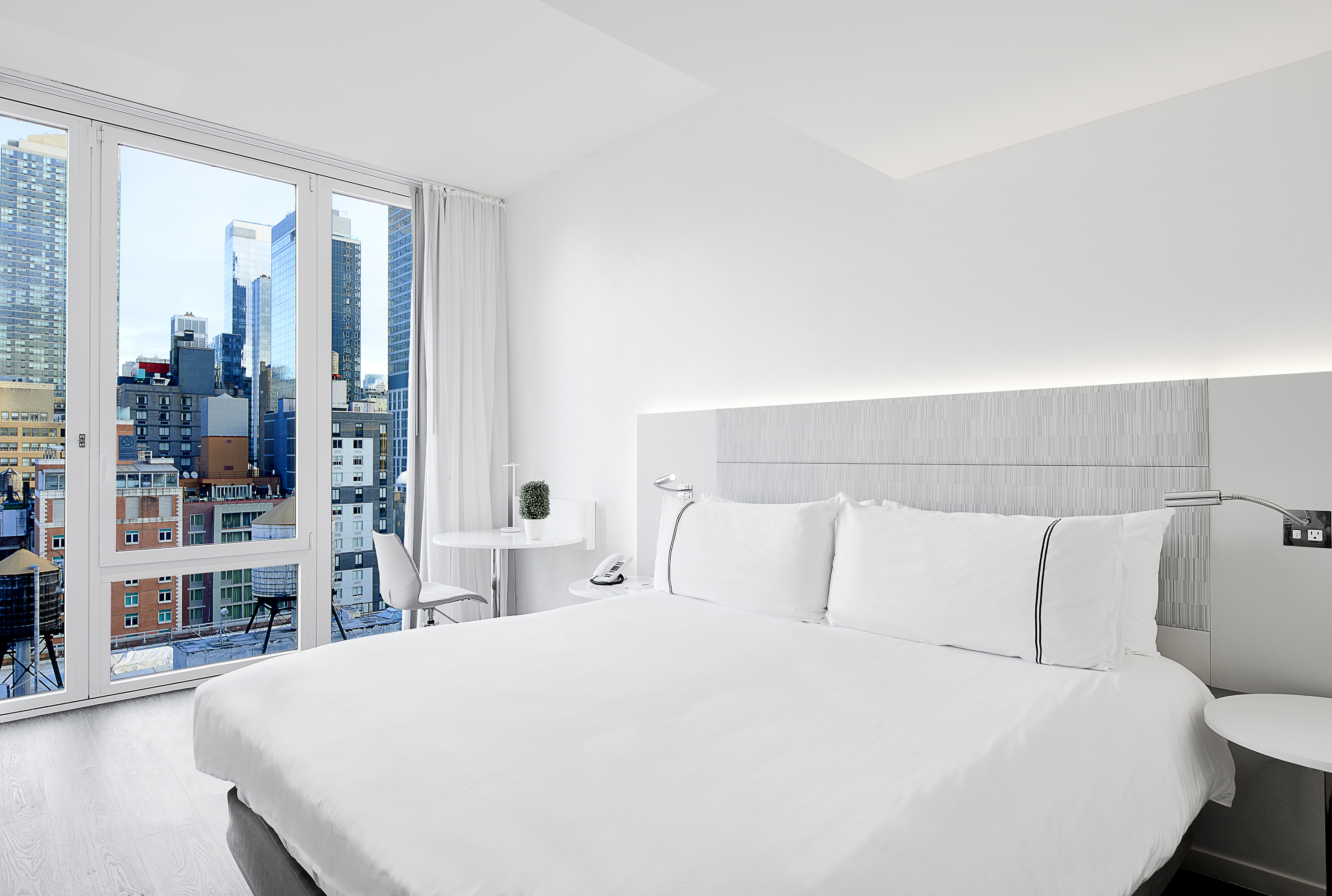 a white bed with white sheets and a table and chairs in a room with a city view