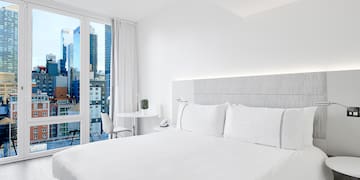 a white bed with white sheets and a table and chairs in a room with a city view
