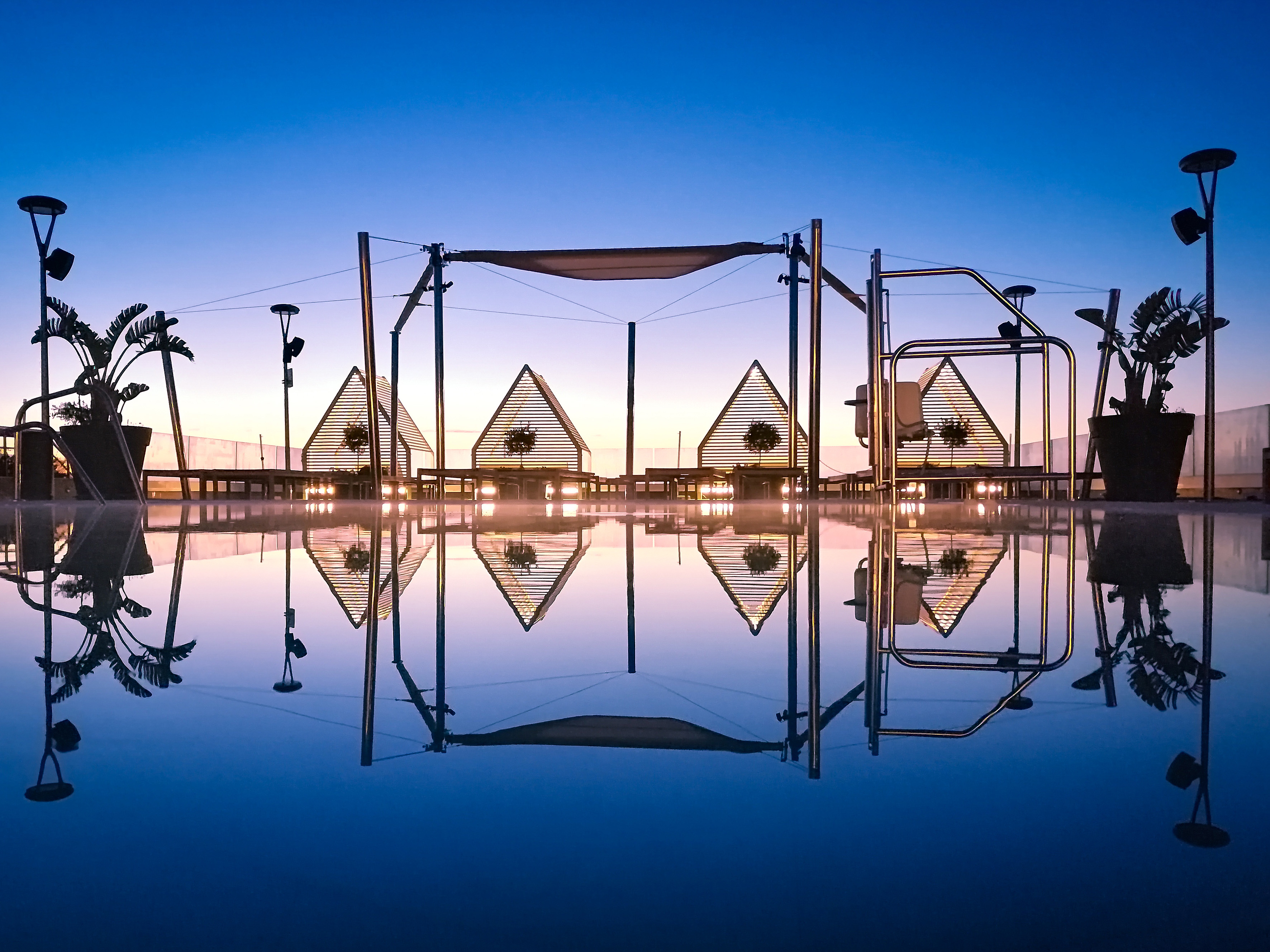 Modern rooftop pool lounge with triangular cabanas reflecting at twilight.