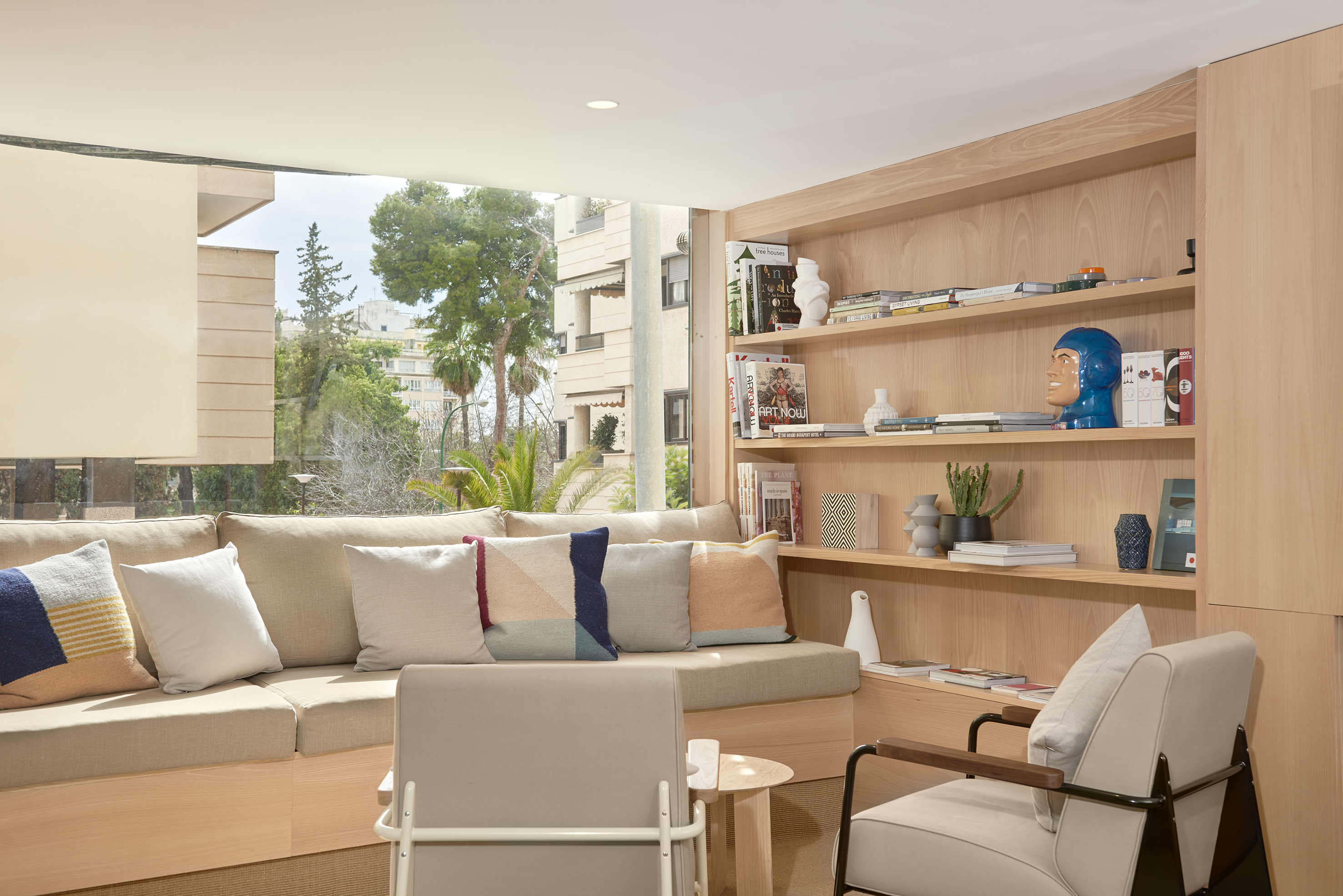 Bright contemporary lounge with built-in sofa, cushions, and wooden shelves.