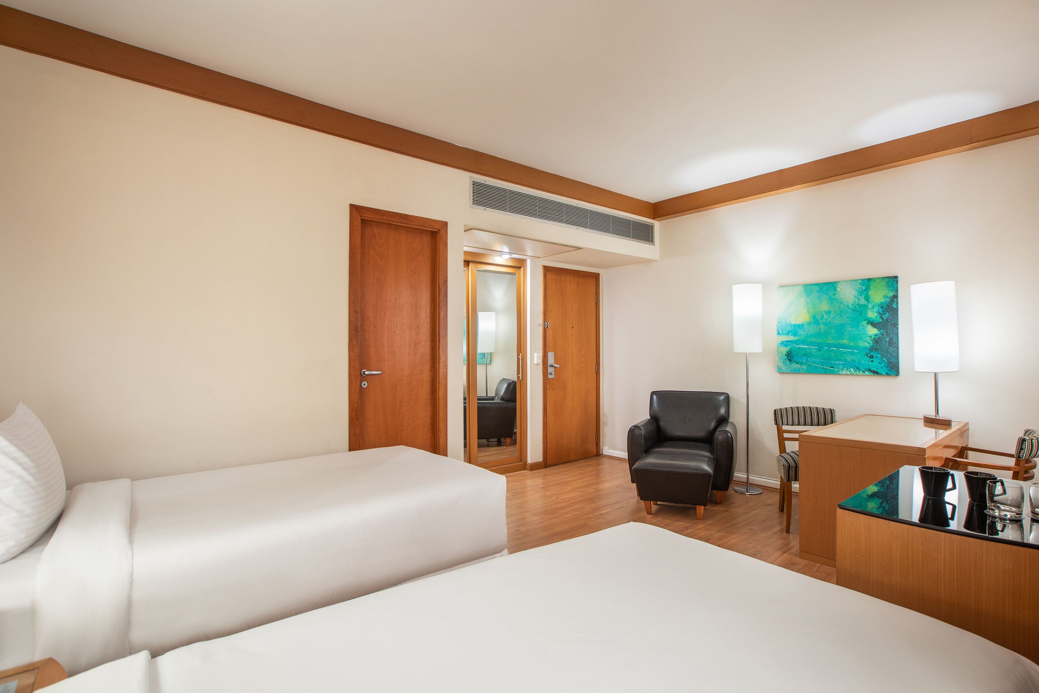 Hotel guest room with twin beds, desk, armchair, and modern decor.