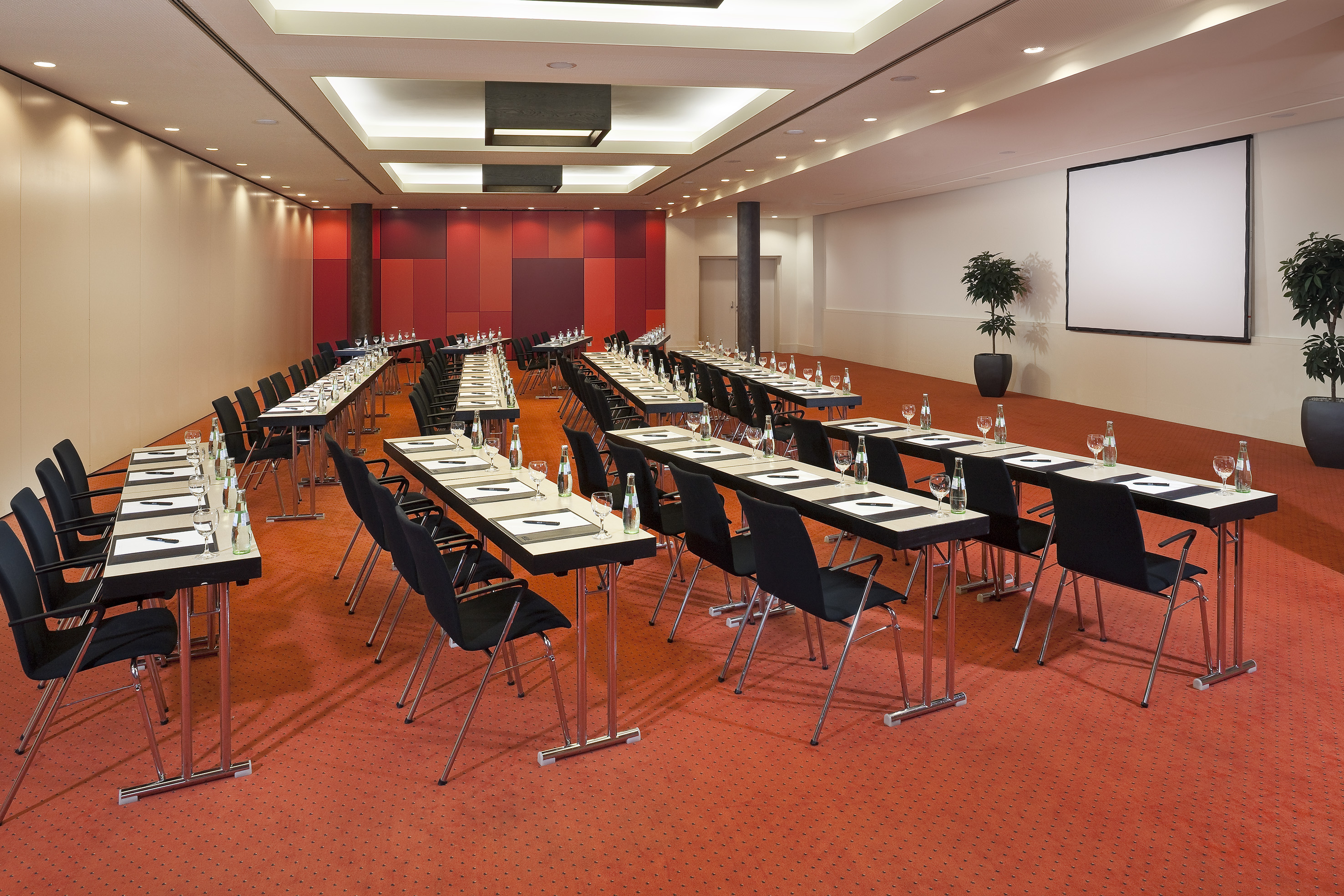 Empty conference room with classroom setup, projector screen, and red carpet.