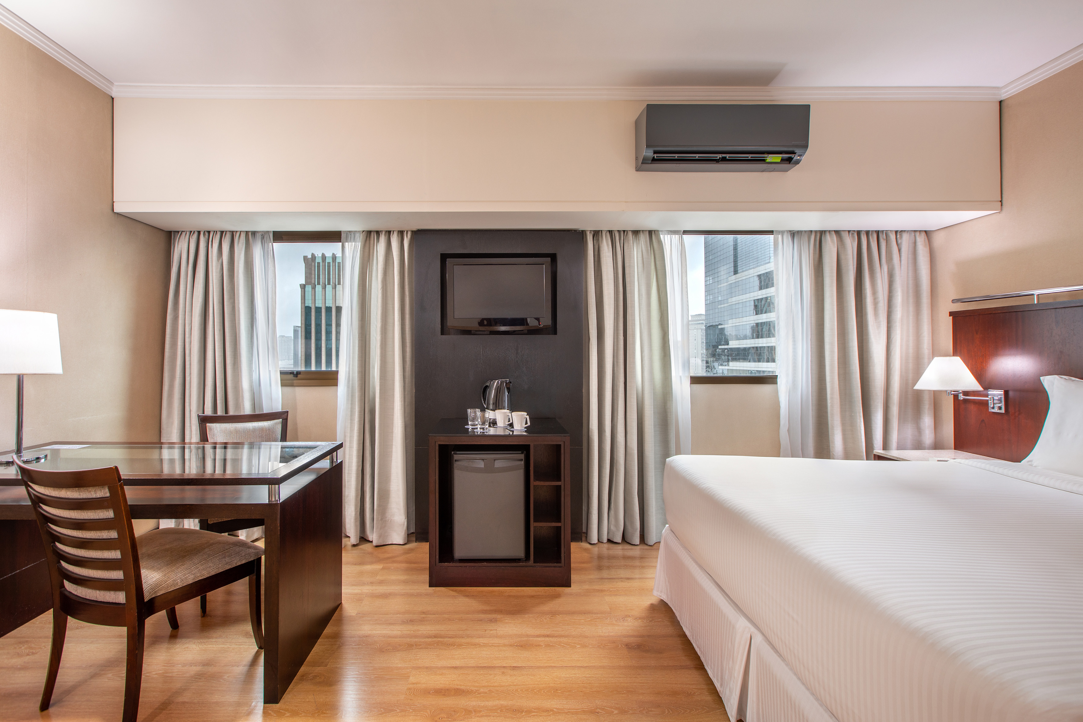 Comfortable hotel room with bed, workstation, TV, mini-bar, and city view.