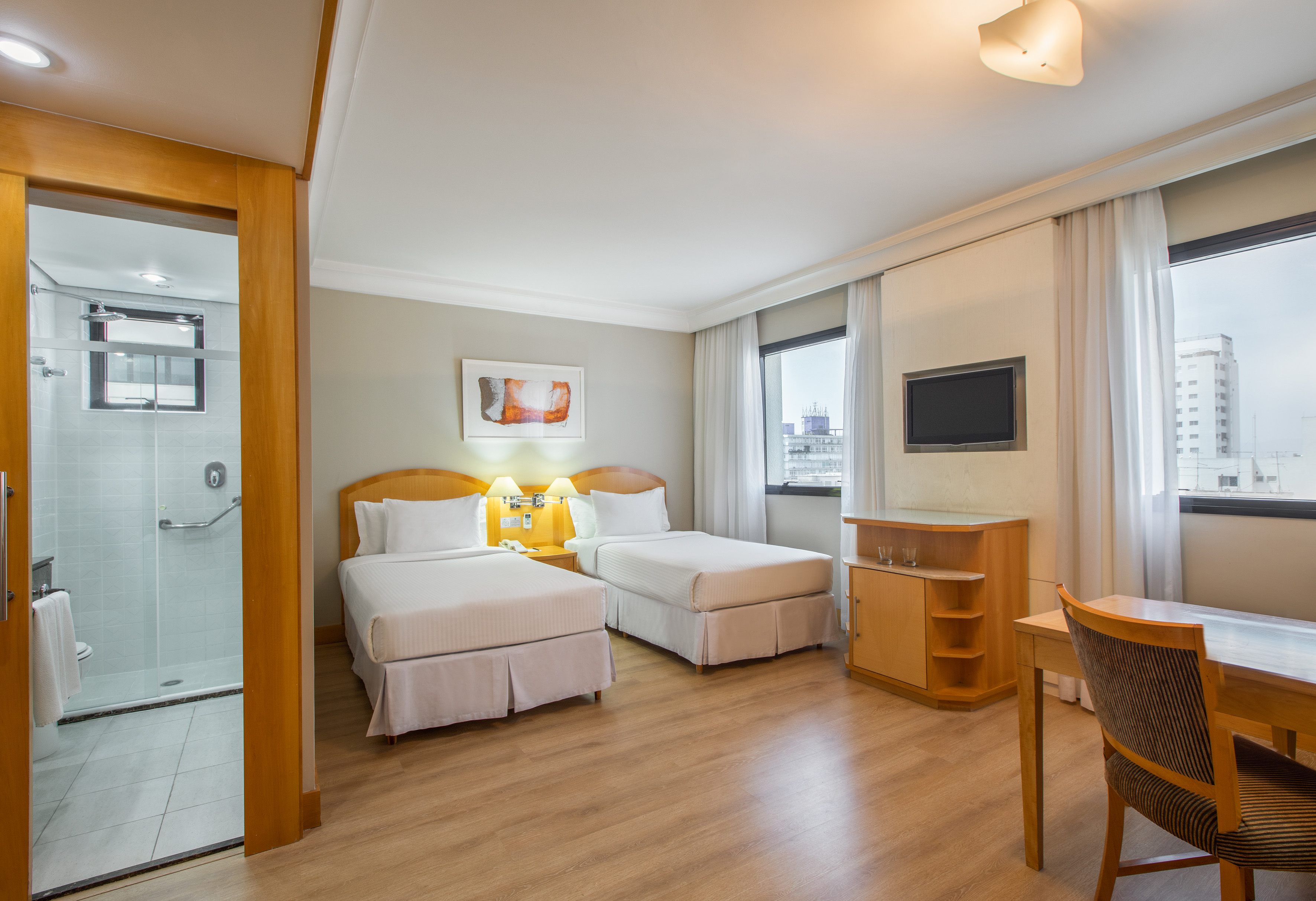 Modern hotel room with twin beds, wooden floor, city view, TV, and shower bathroom.