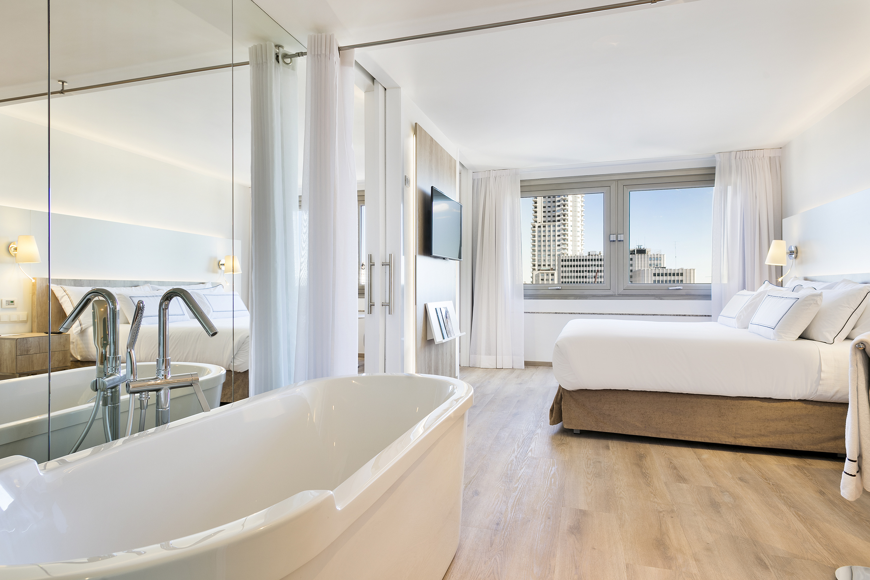 Modern hotel room with integrated bathtub, large bed, and city view.