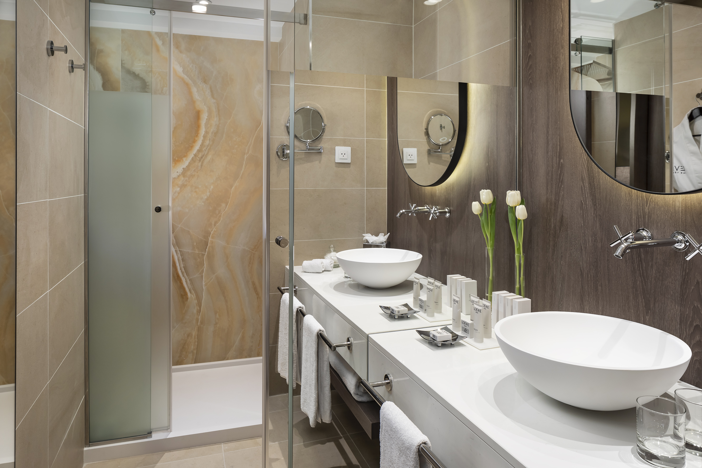 Contemporary hotel bathroom featuring double vanity, vessel sinks, and a marble shower.