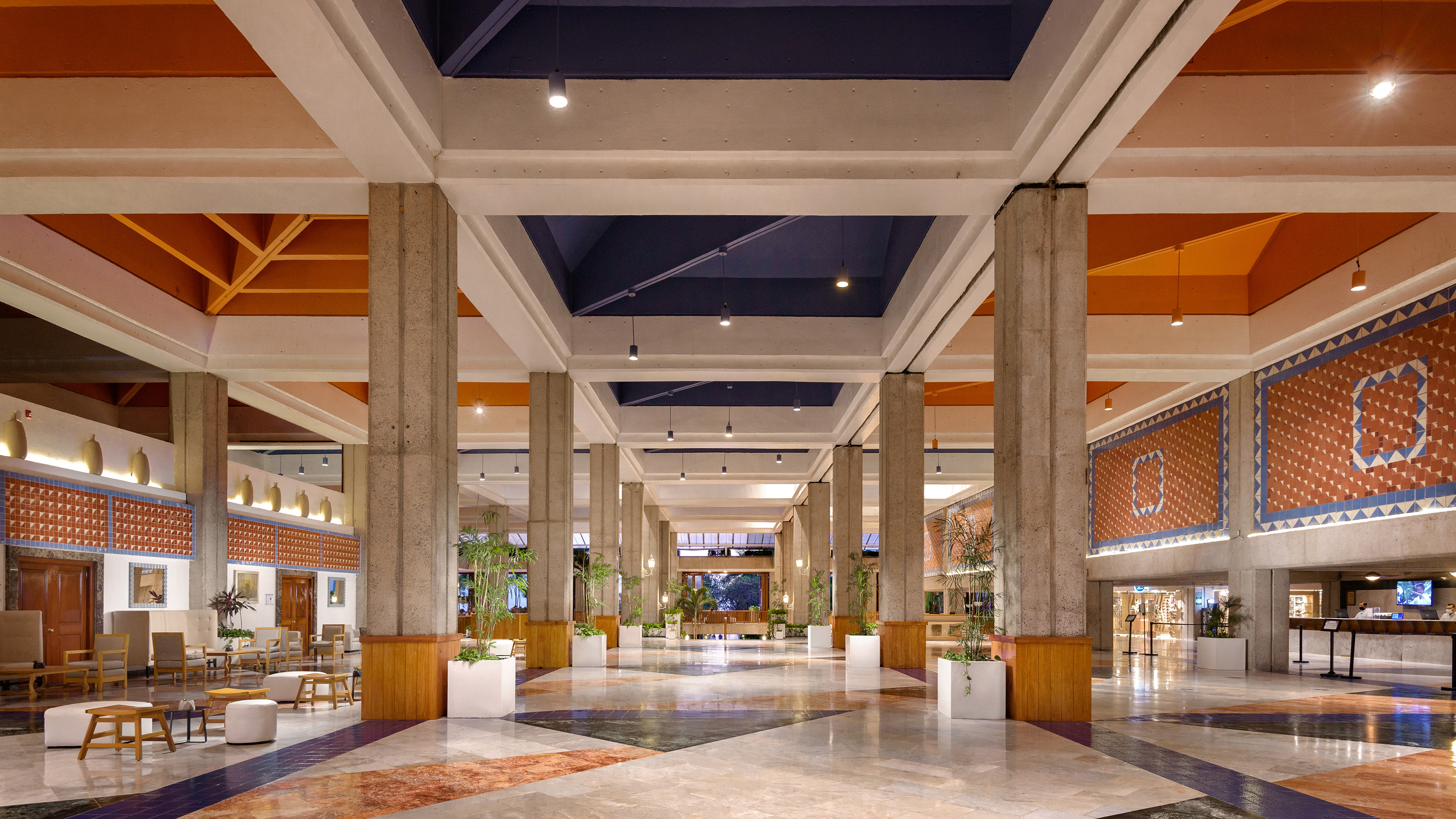 Hotel lobby, concrete columns, orange/blue mosaic walls, and patterned marble floor.
