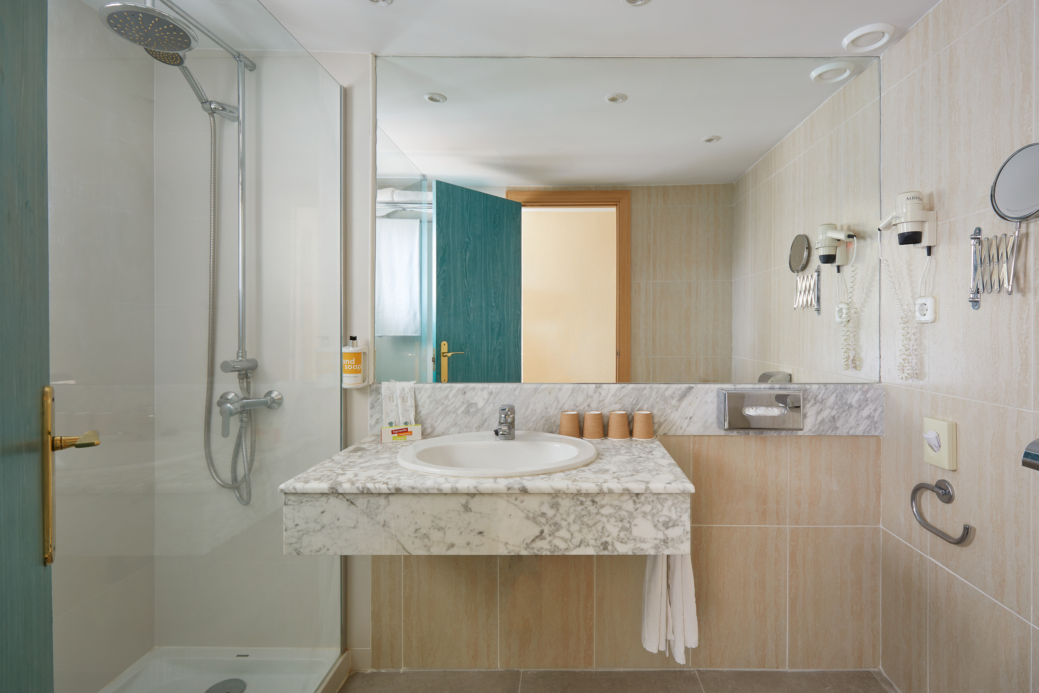 Modern hotel bathroom with shower, marble vanity, sink, and mirror.
