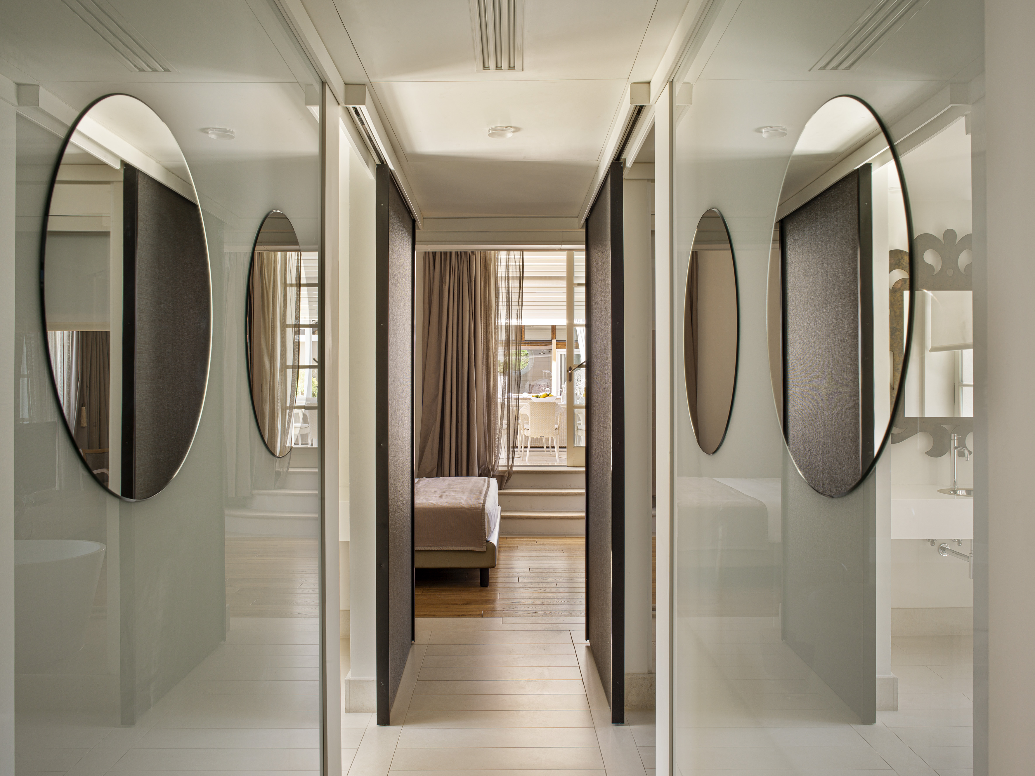 Modern hotel hallway with mirrors reflecting bedroom and bathroom, leading to patio.