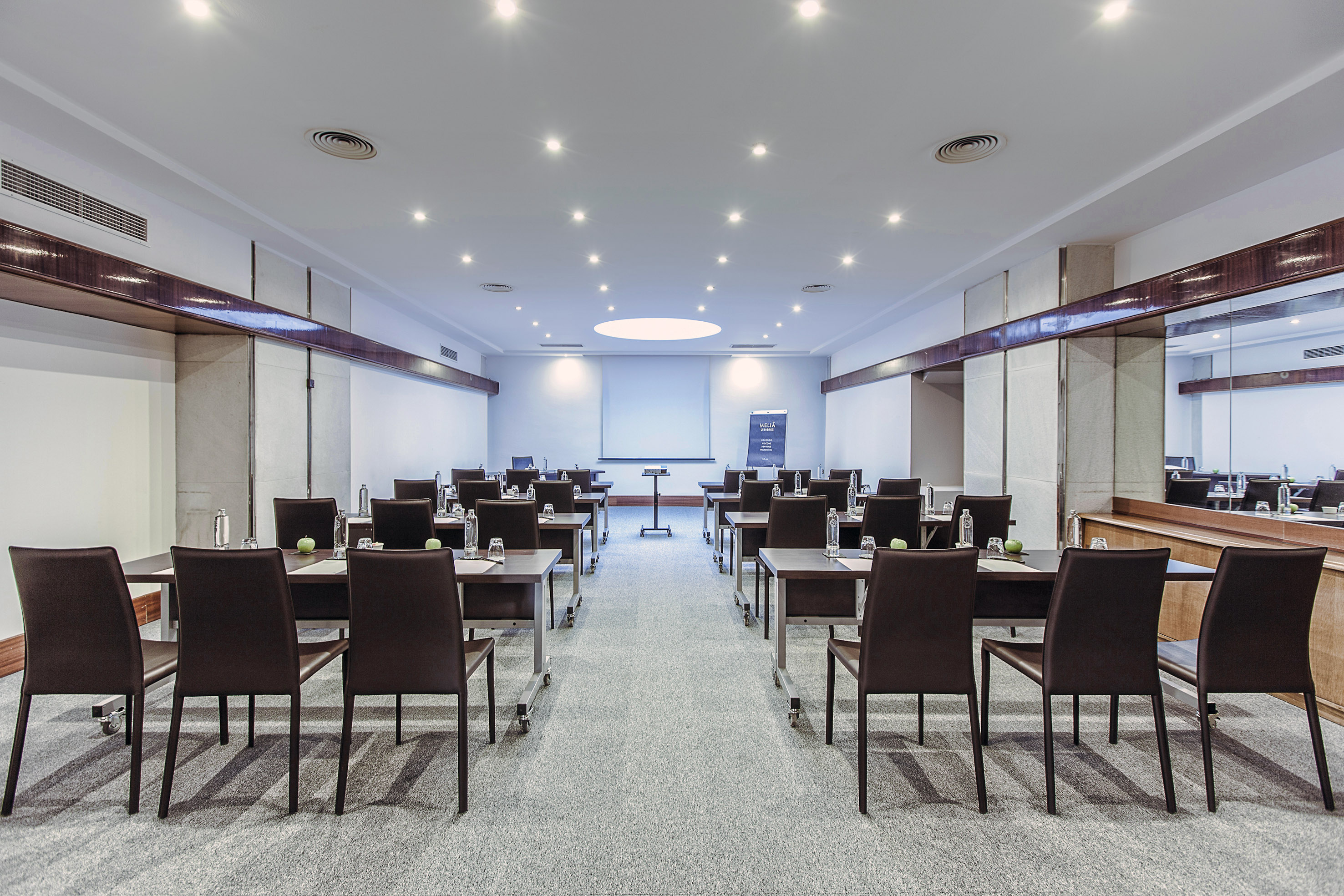 Modern hotel conference room setup with tables, chairs, and projector screen.