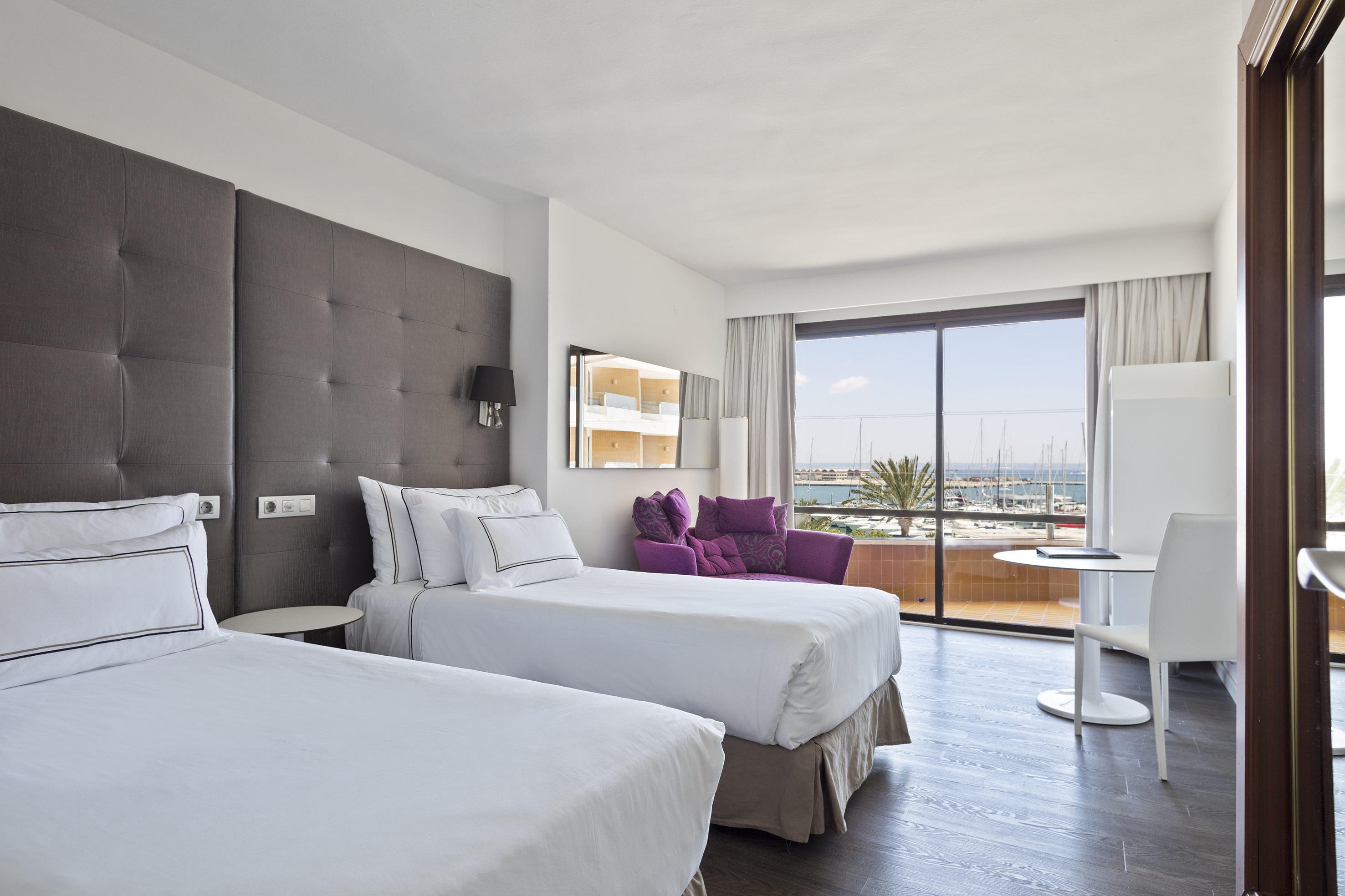 Modern hotel room with twin beds, marina view balcony, and purple armchair.