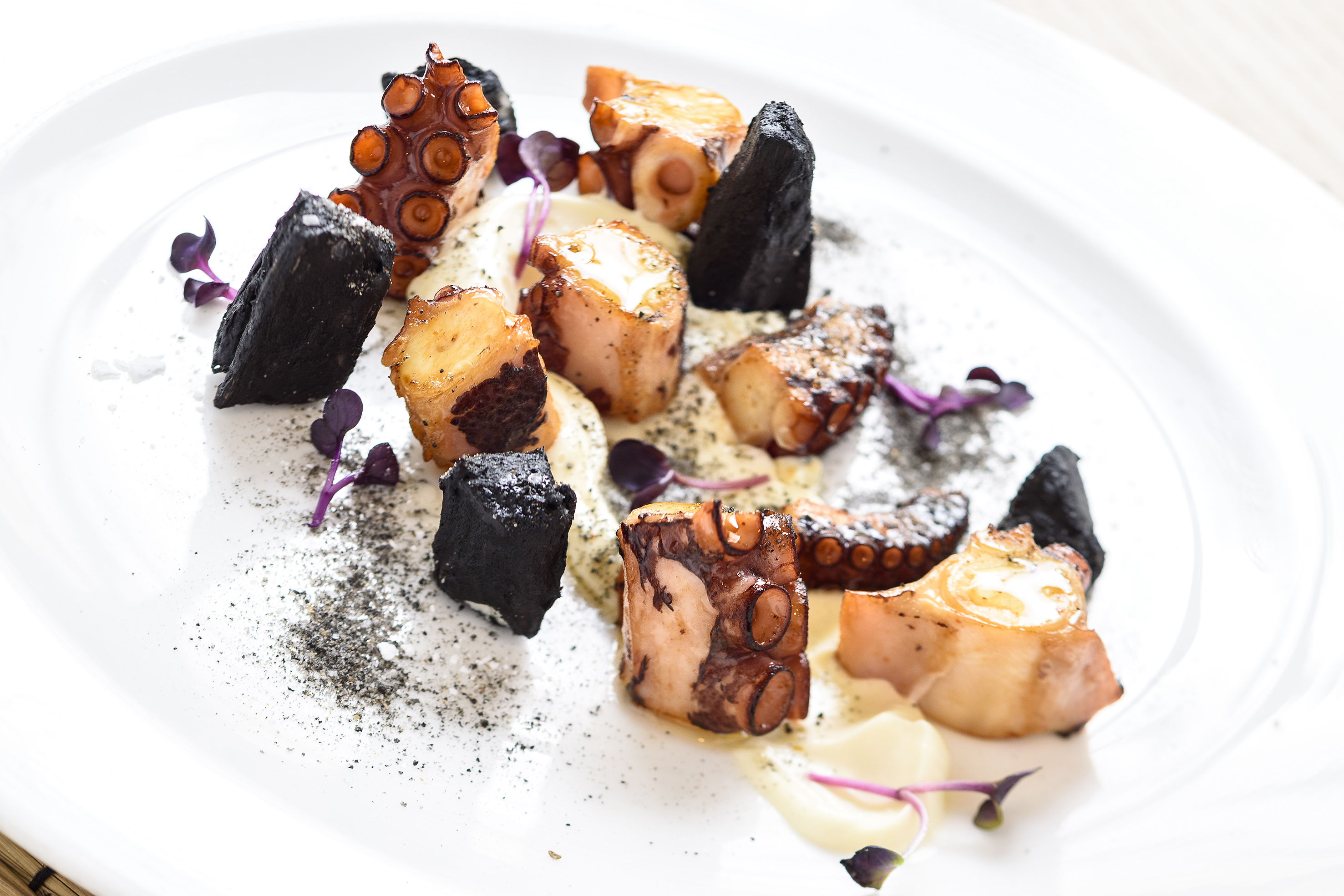Gourmet grilled octopus, black fritters, cream sauce, and purple garnish.