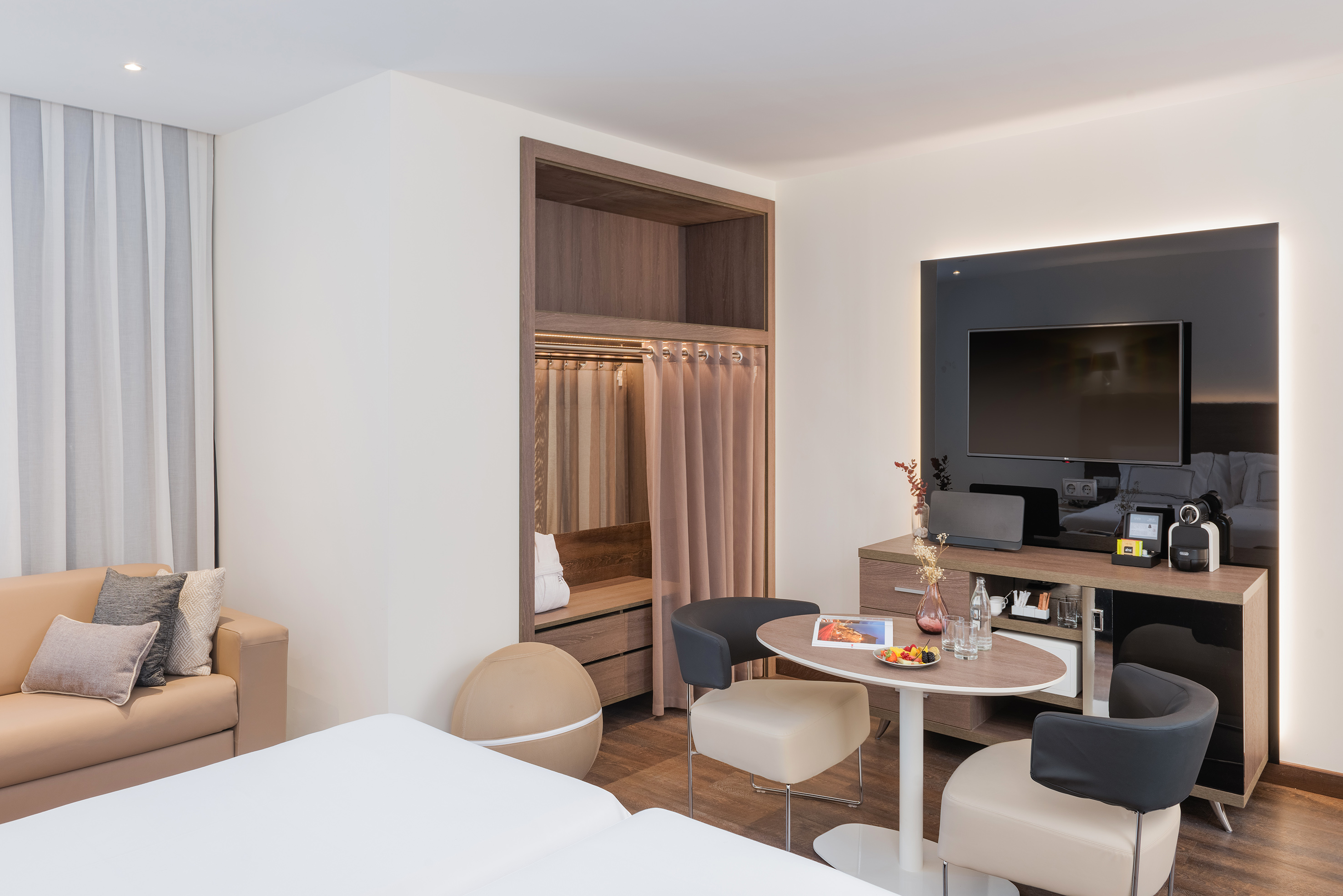 Modern hotel room with bed, sofa, dining, TV, and open closet.
