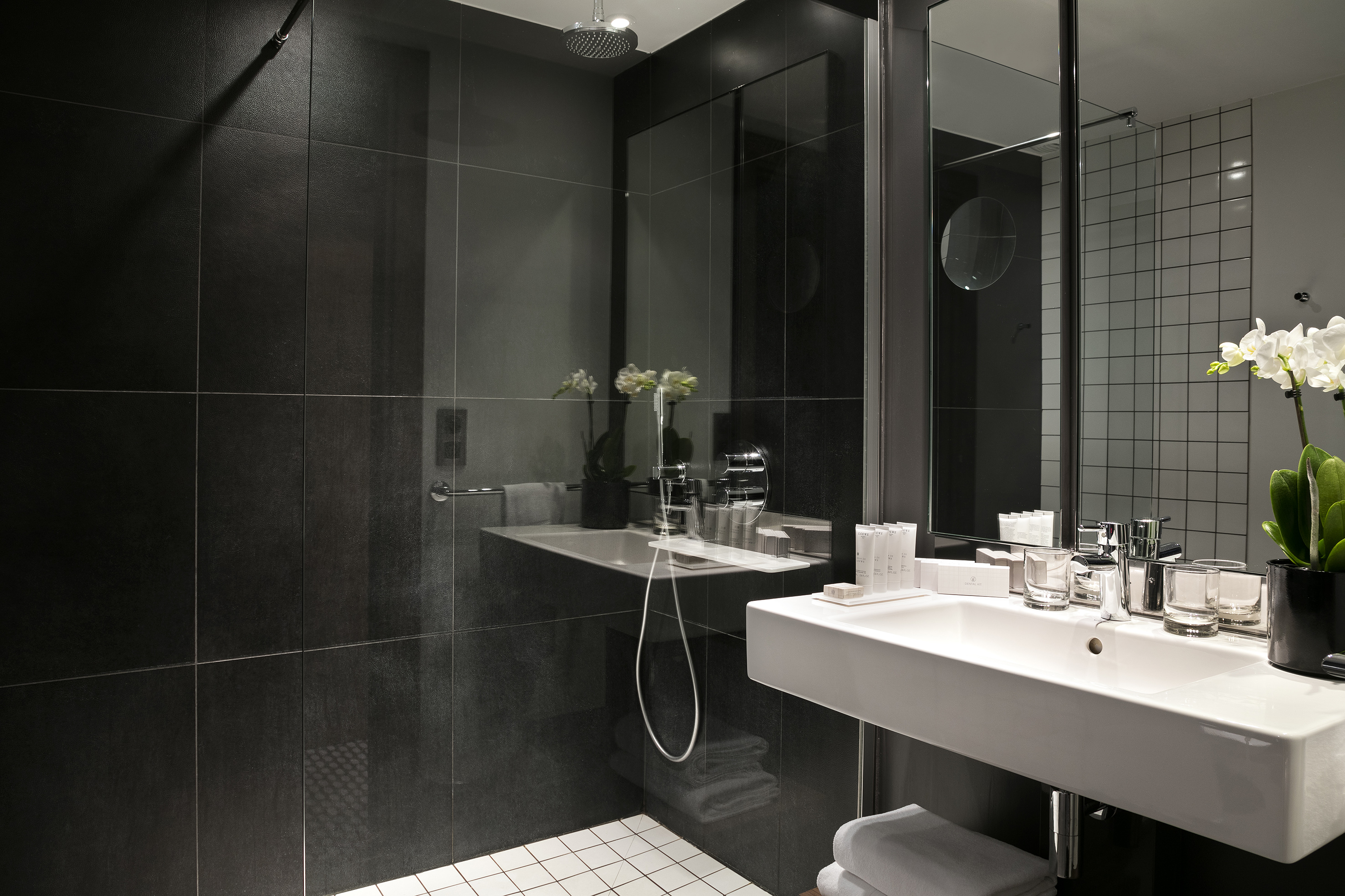 Modern hotel bathroom with black tiled shower and white vanity sink.