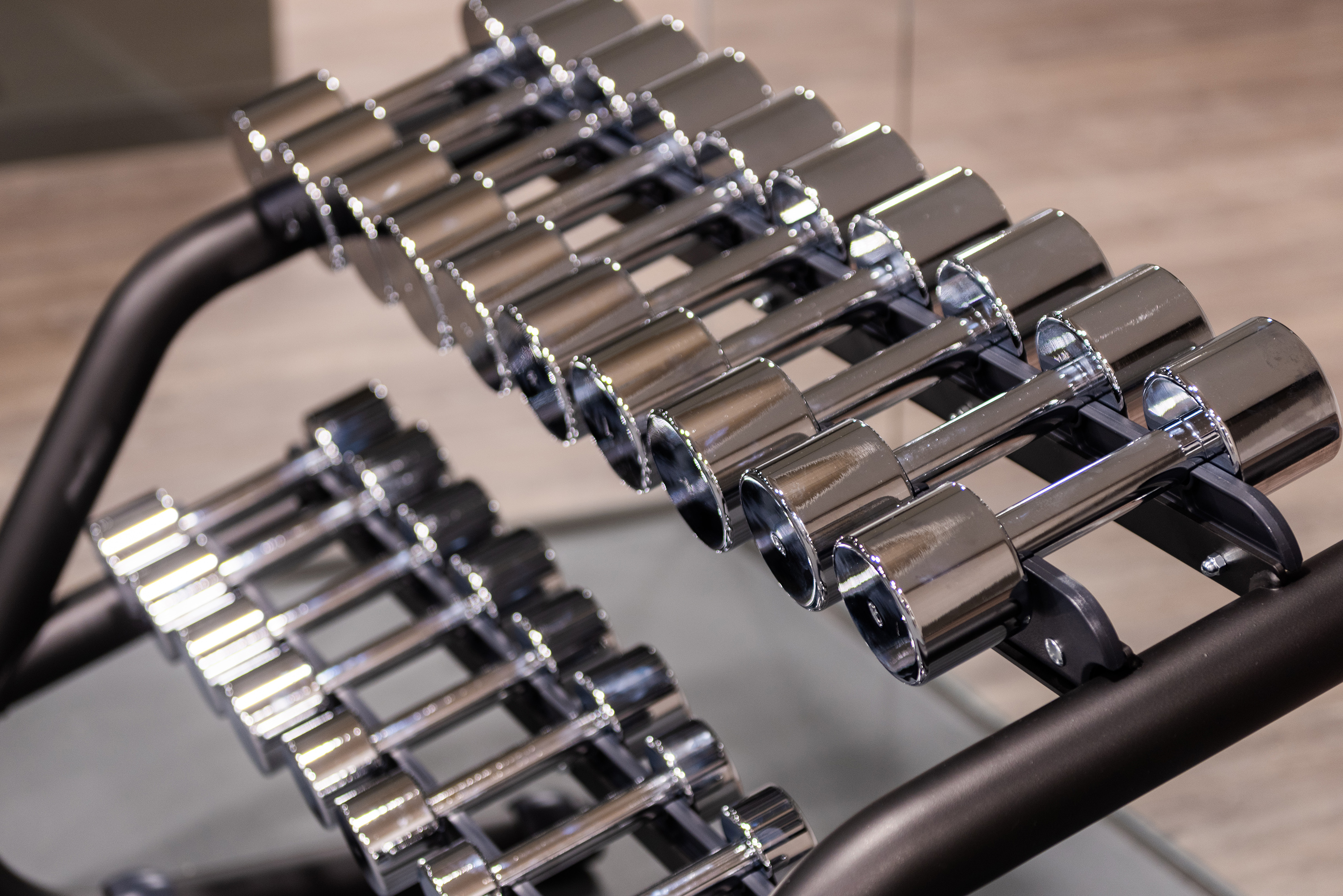 Rows of shiny chrome dumbbells on a black gym rack for weightlifting.
