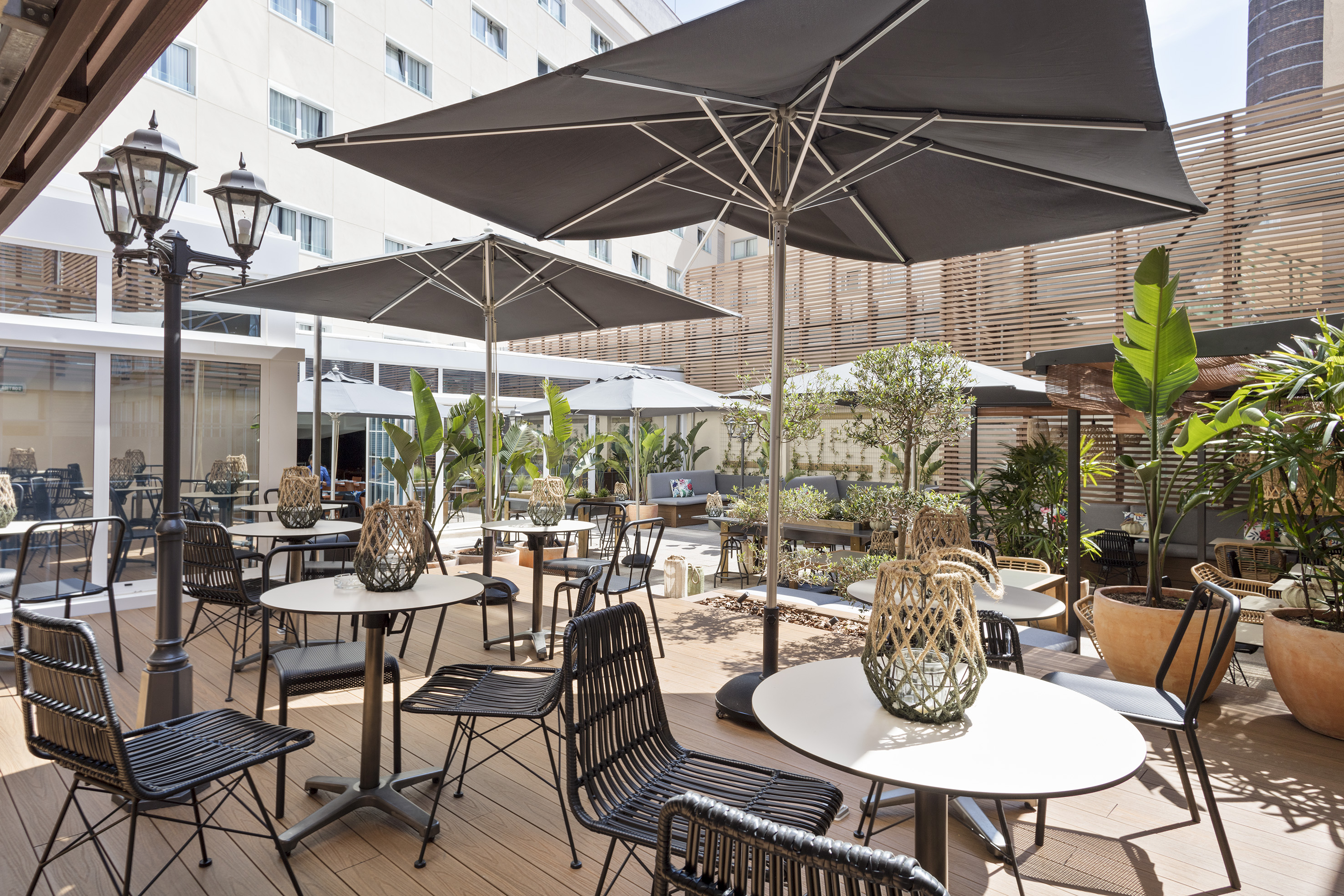 Outdoor hotel terrace with black tables, chairs, umbrellas, and green plants.