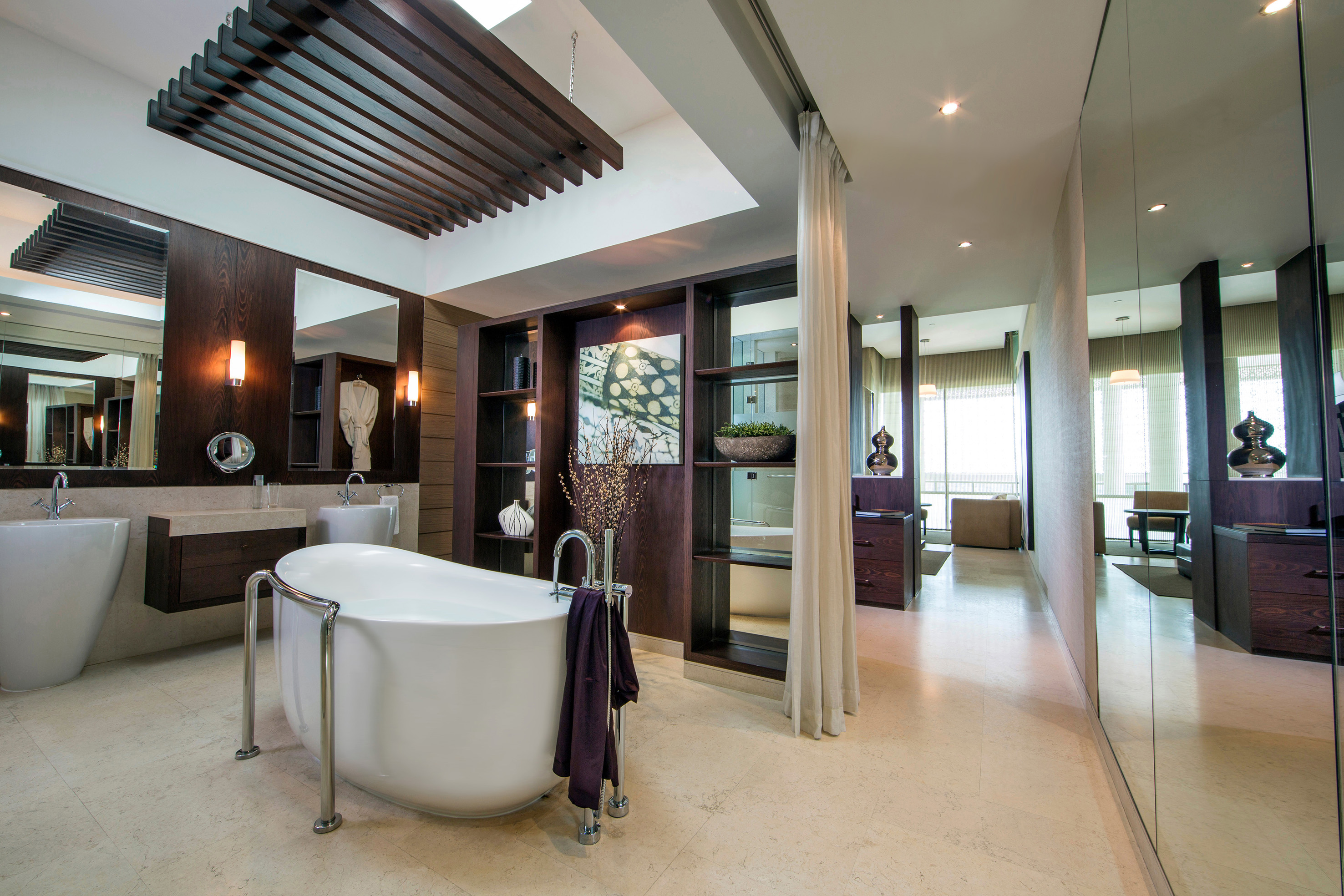 Modern spa bathroom with freestanding tub, dual vanity, dark wood, and sleek design.