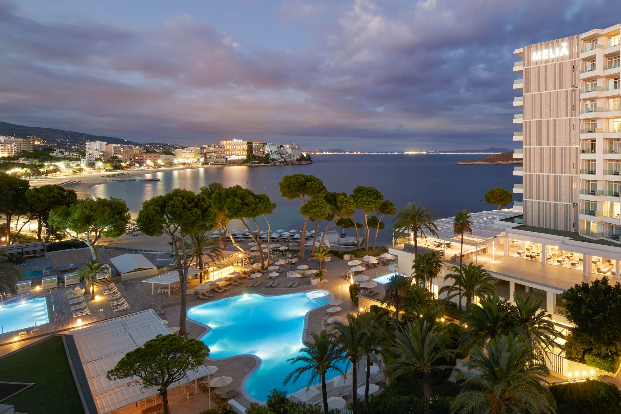 Meliá beachfront resort with illuminated pools and ocean view at dusk.