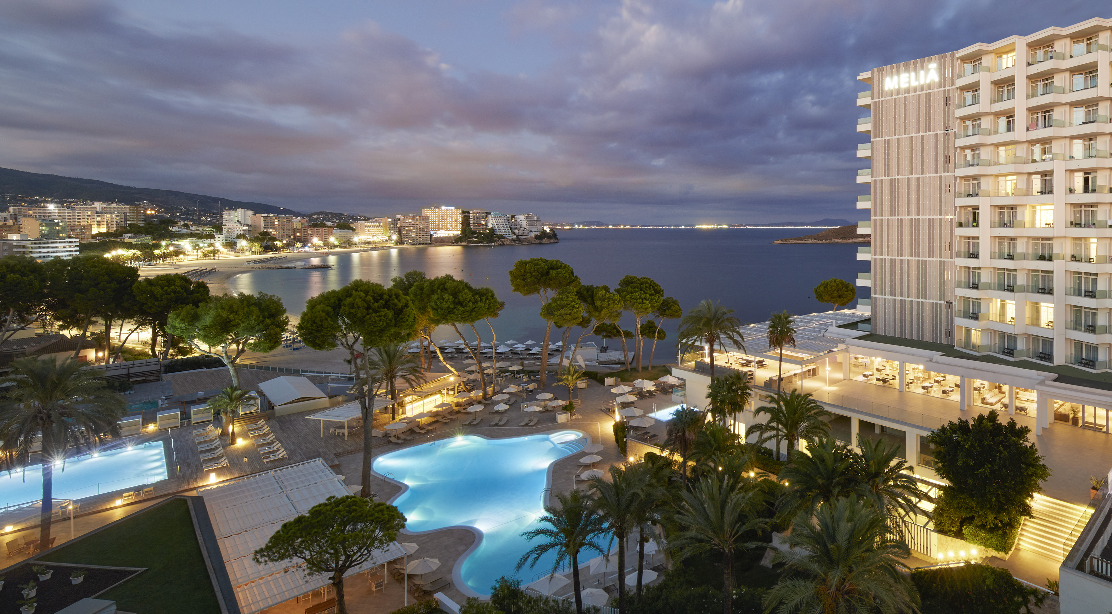 Meliá beachfront resort with illuminated pools and ocean view at dusk.