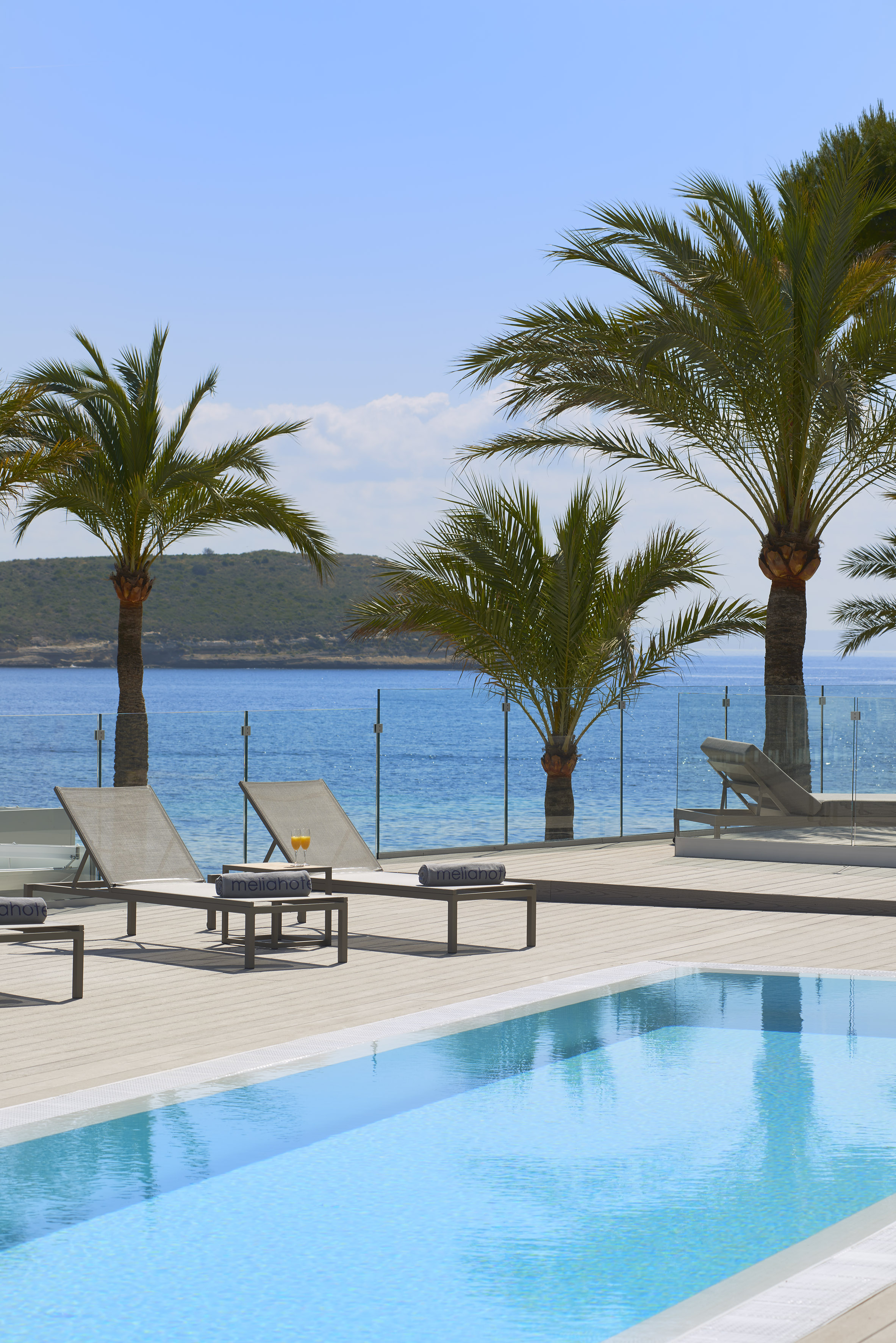 Meliá hotel pool deck, sun loungers, palm trees, and clear blue sea.
