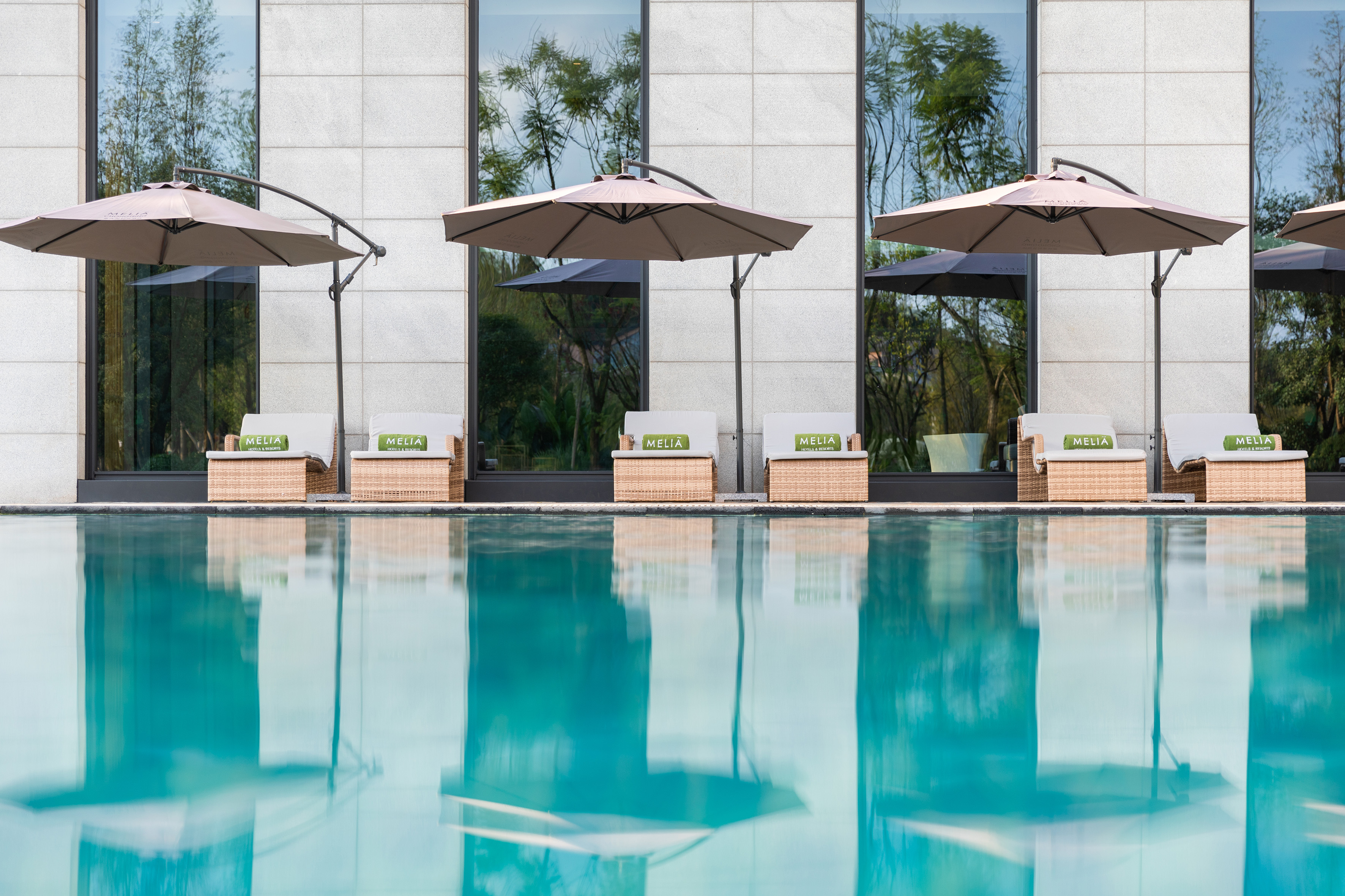 Meliá resort pool with wicker loungers, green towels, and shade umbrellas.