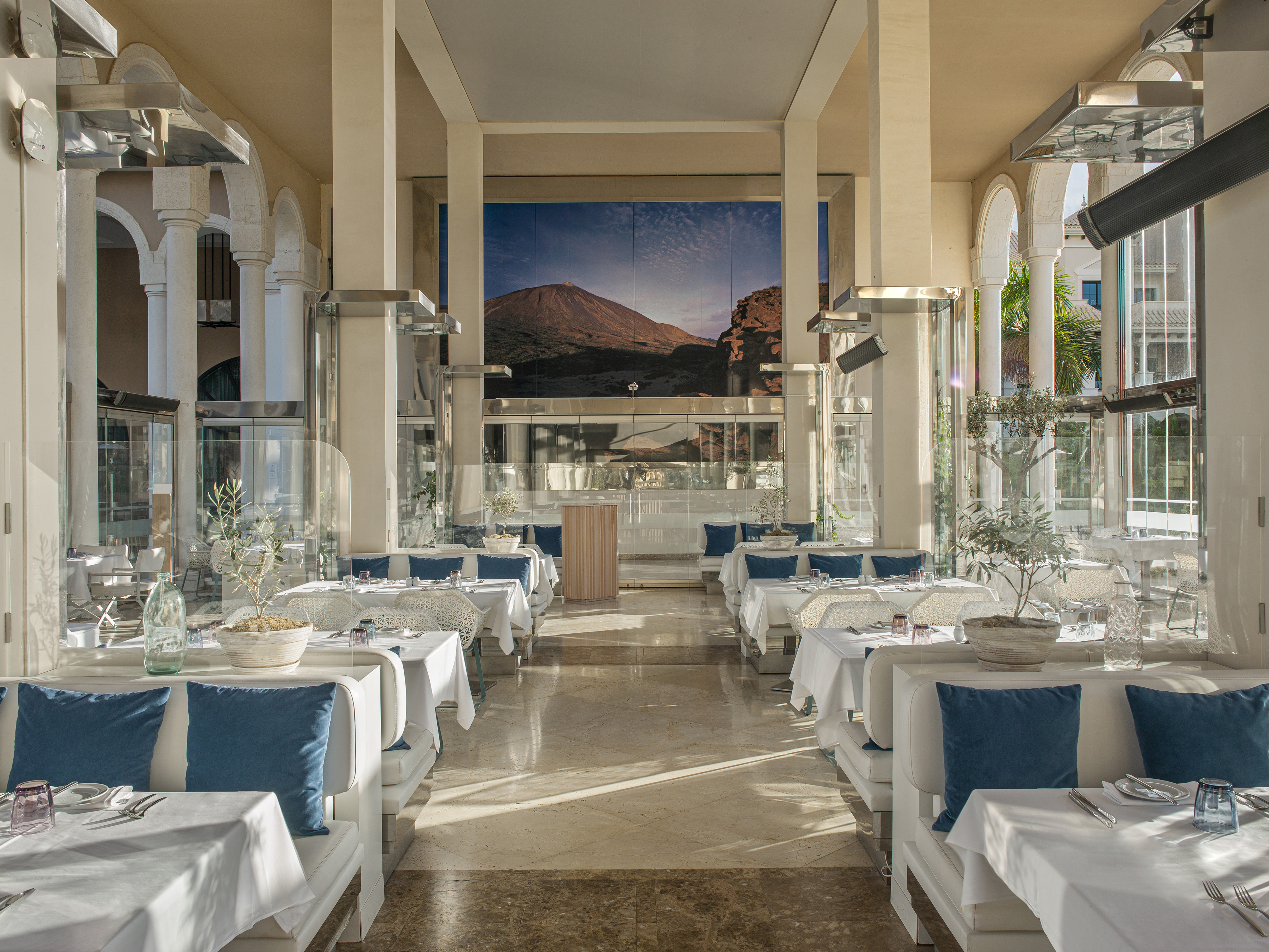 Elegant restaurant interior with white tables, blue cushions, and mountain mural.