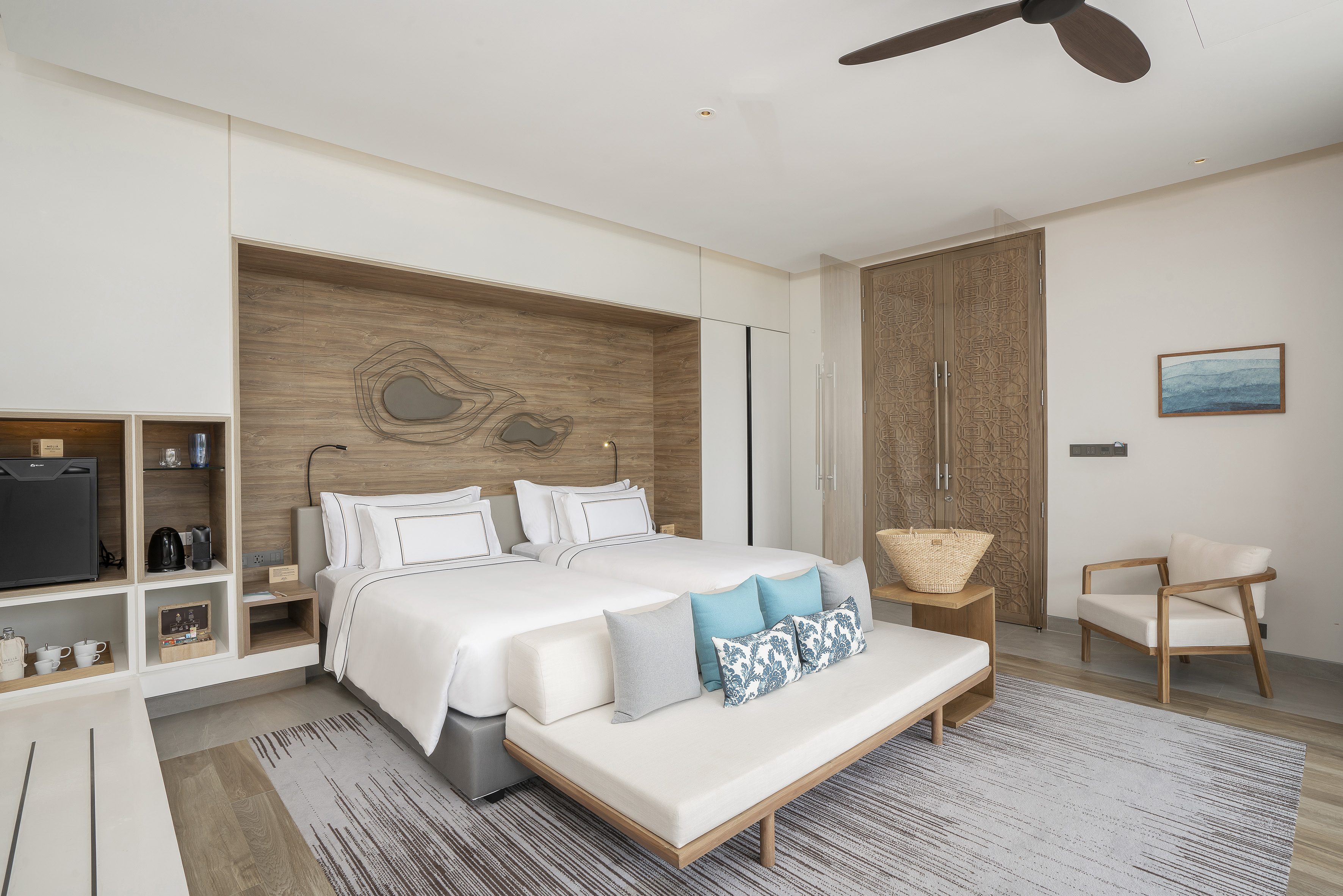 Modern hotel room with twin beds, wooden headboard, and stylish daybed.