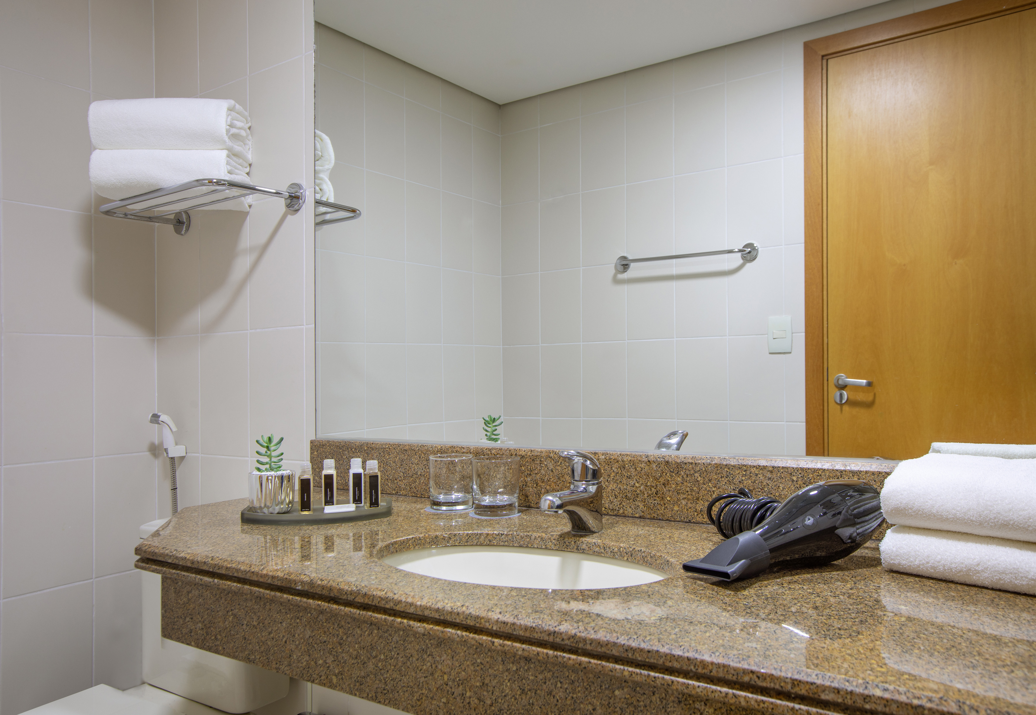 Hotel bathroom with granite vanity, sink, mirror, towels, hairdryer, and toiletries.