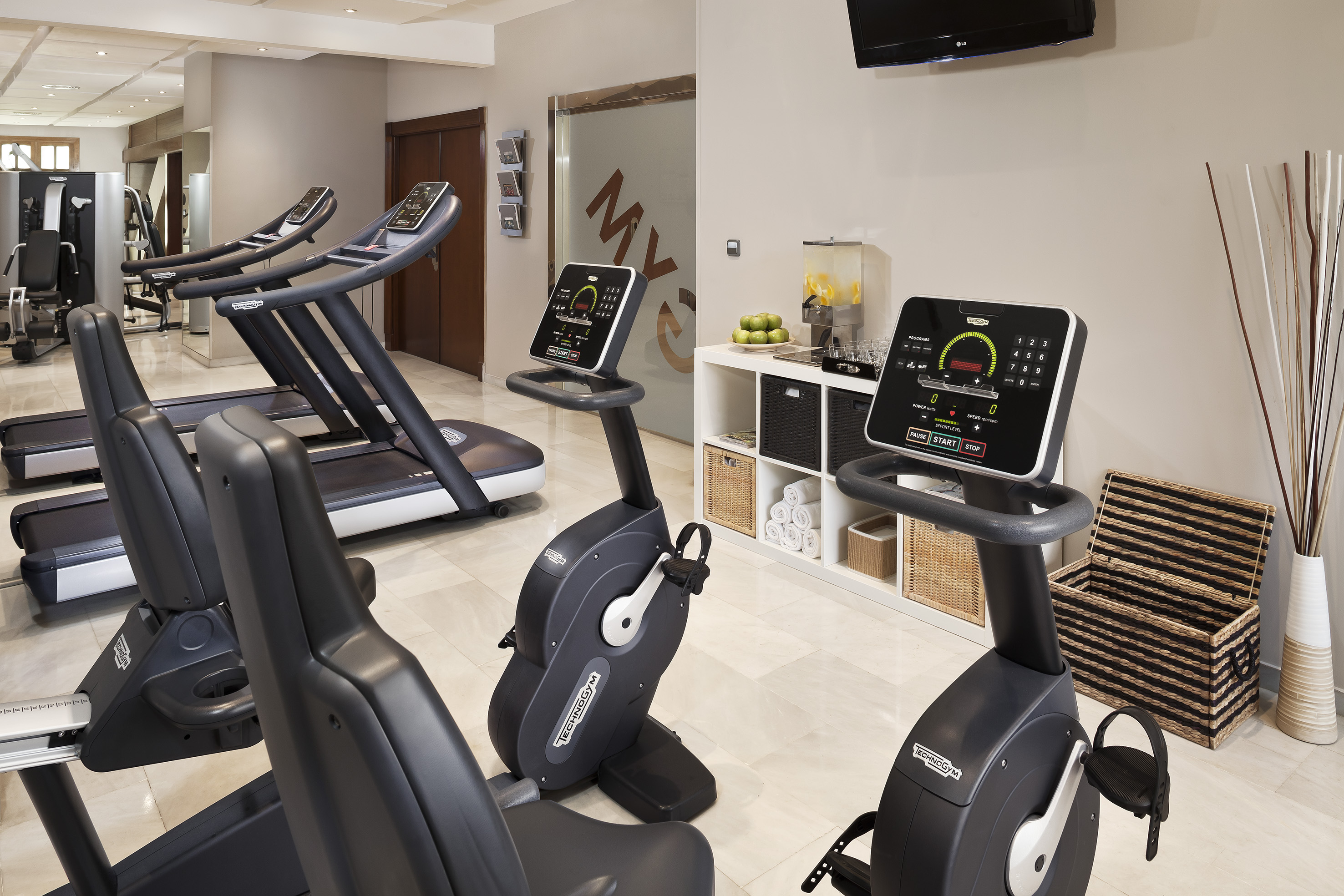 Modern gym with Technogym treadmills, stationary bikes, and refreshment area.