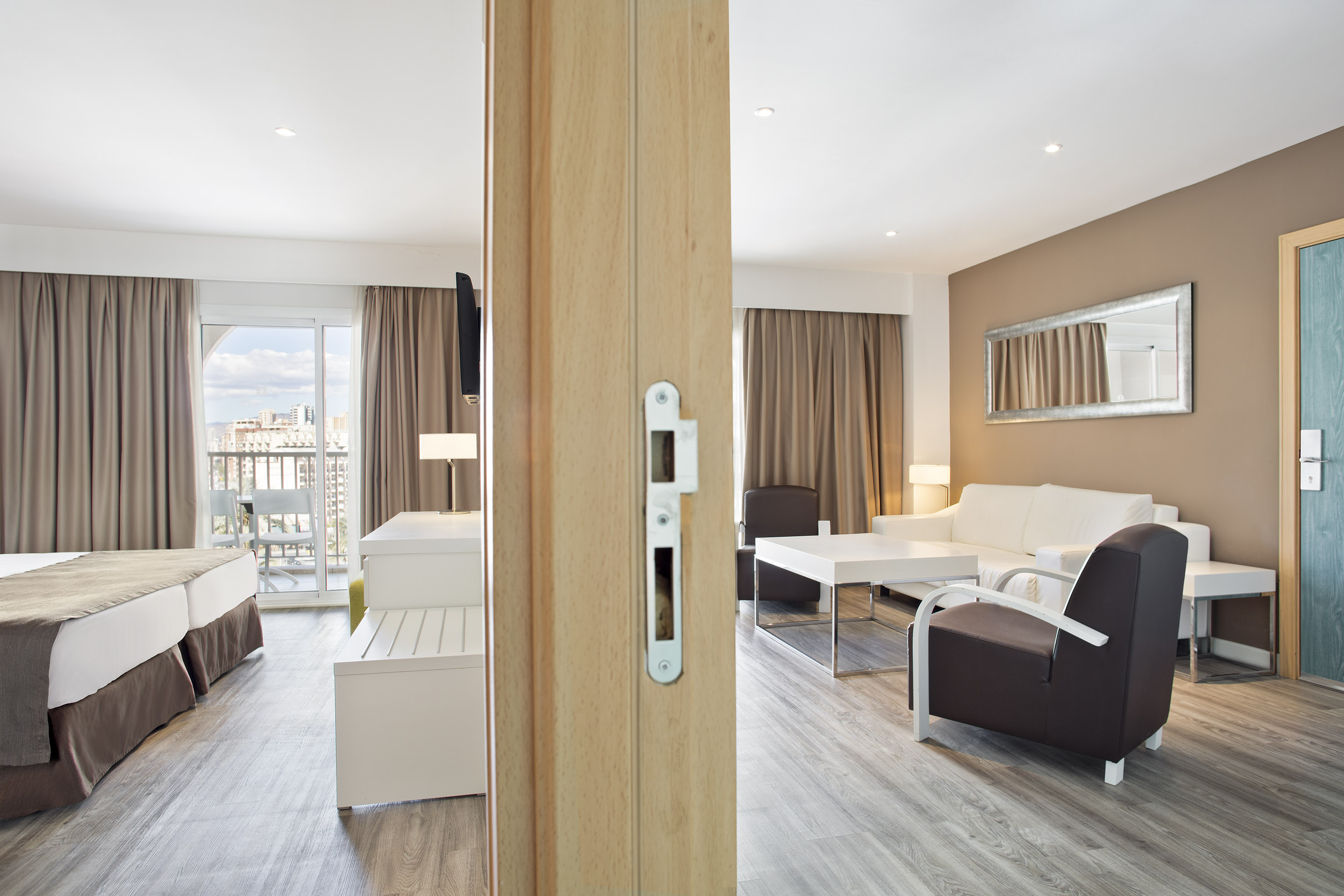Contemporary hotel suite with bedroom, living area, balcony, and wooden floors.