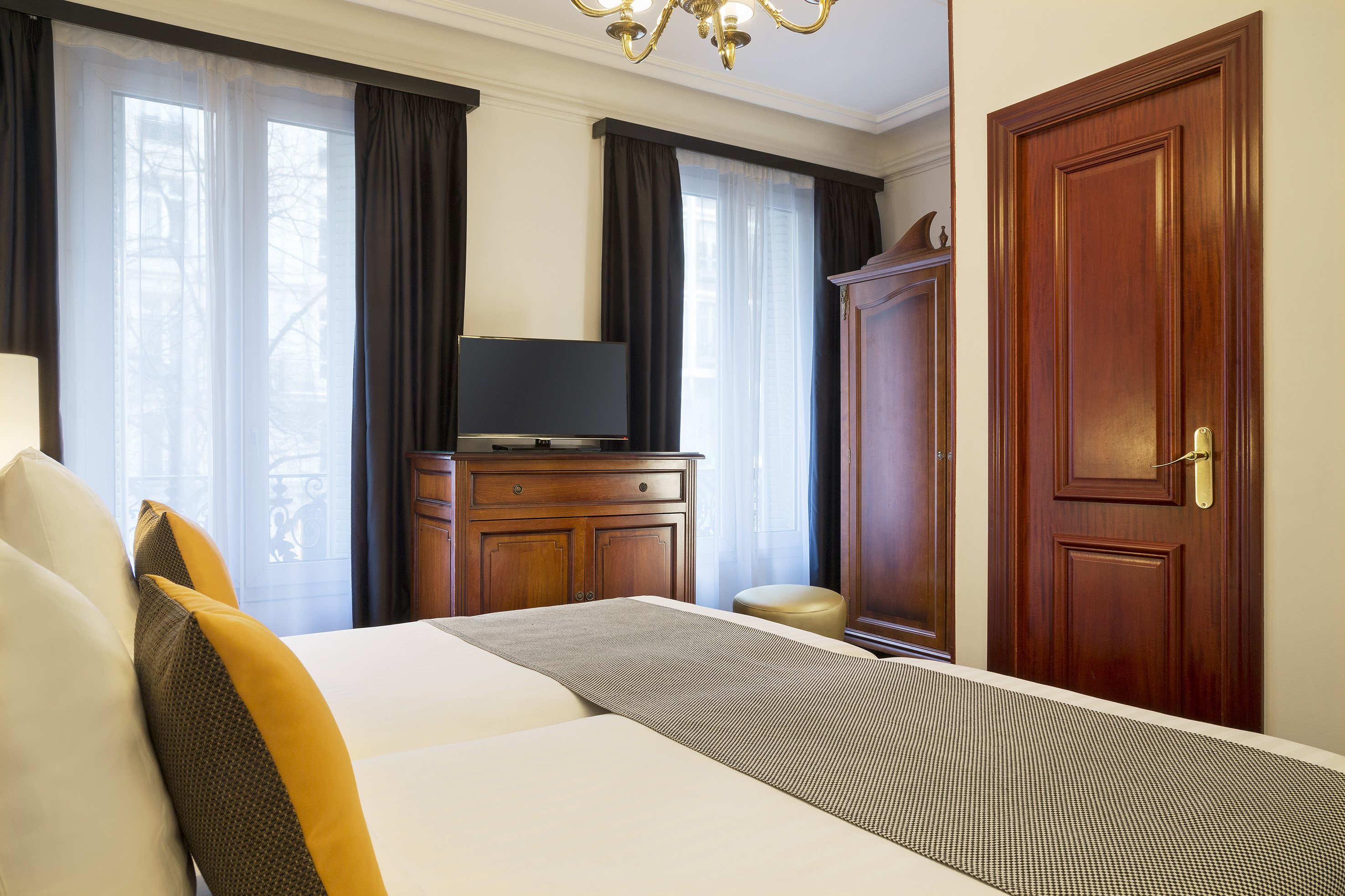 Elegant hotel room with twin beds, wooden furniture, TV, and large windows.