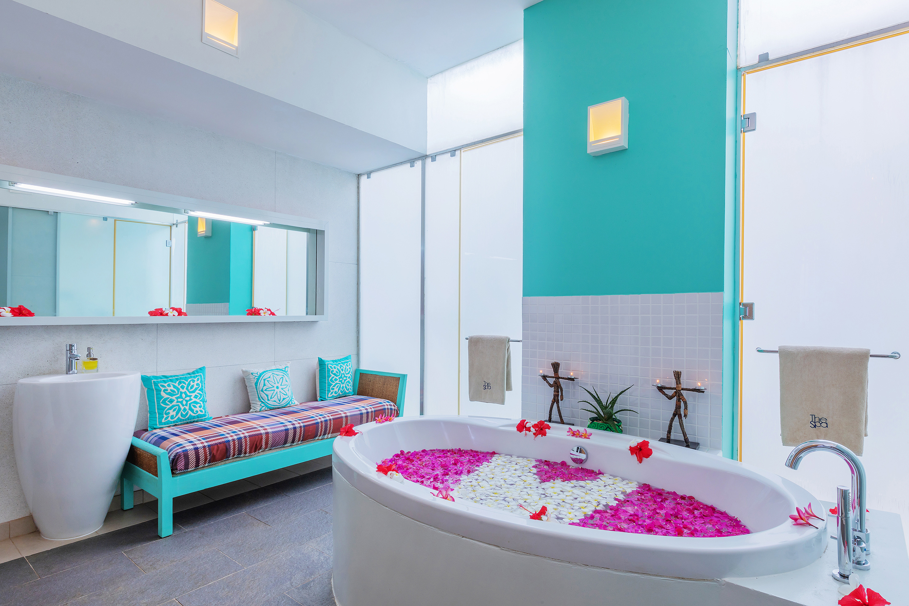 Luxury spa bathroom with petal-filled bathtub, teal accent wall, and relaxation bench.