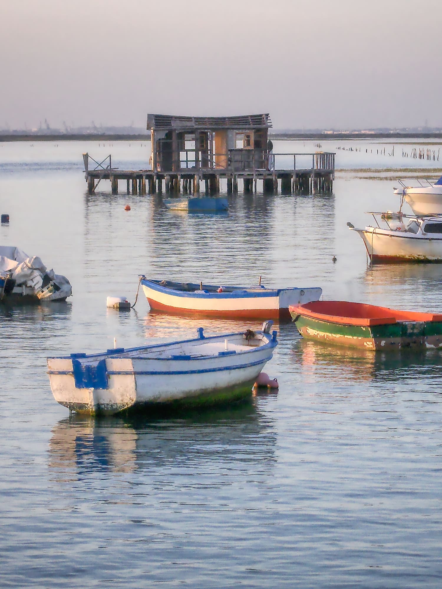 Boats anchored in a calm bay with a rustic wooden stilt shack.
