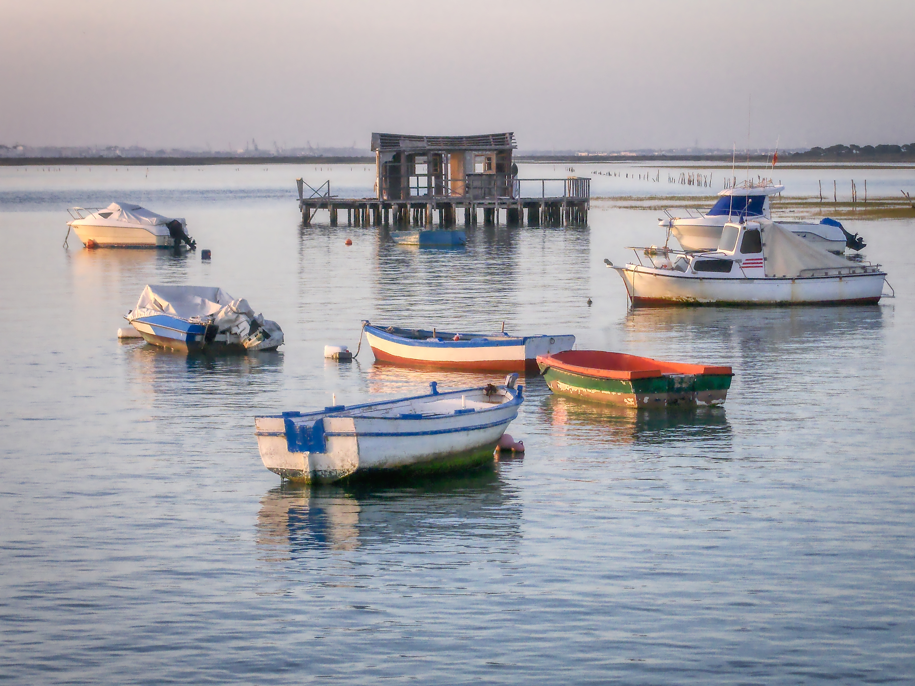 Boats anchored in a calm bay with a rustic wooden stilt shack.