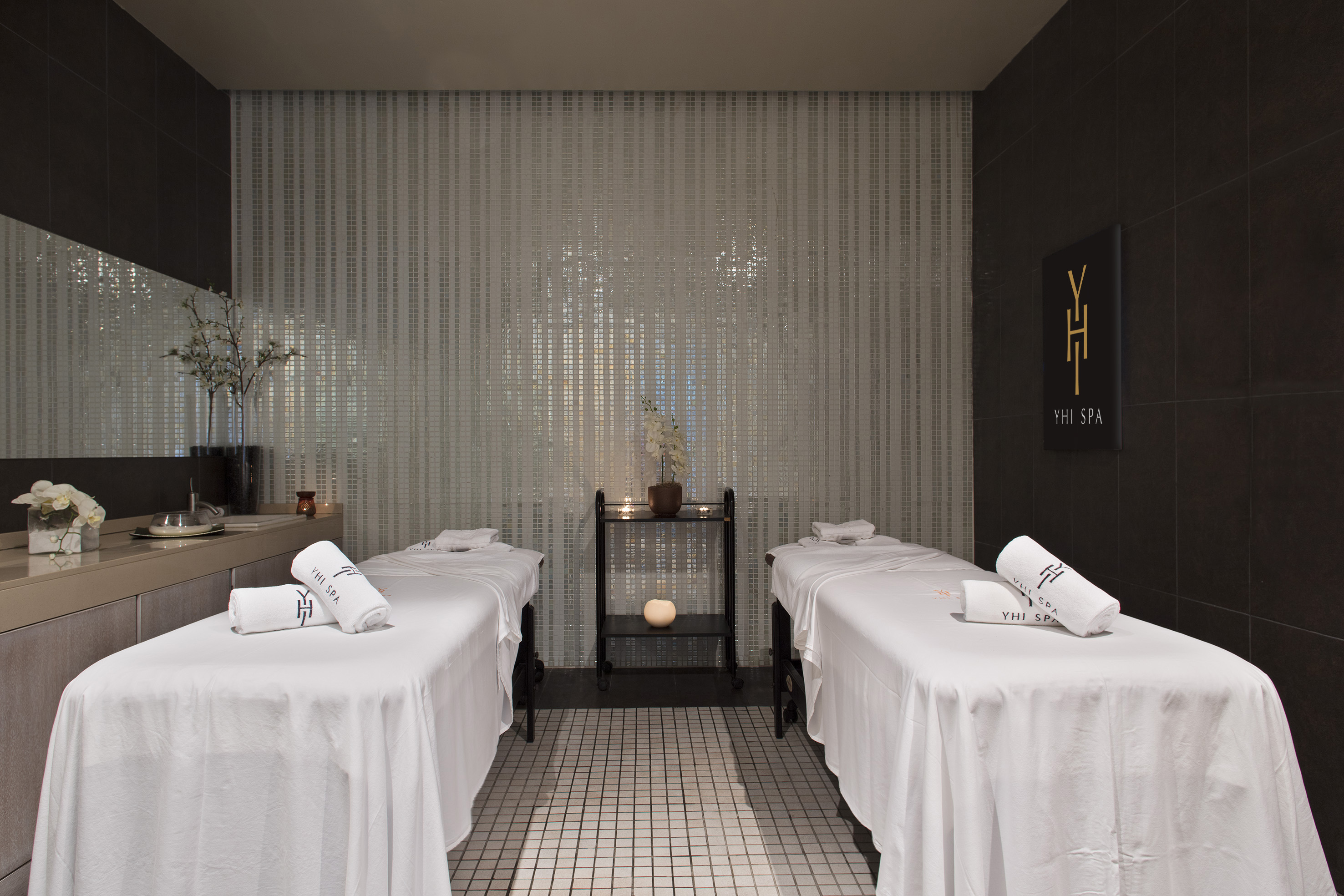 Luxury YHI SPA massage treatment room with two beds and tiled walls.