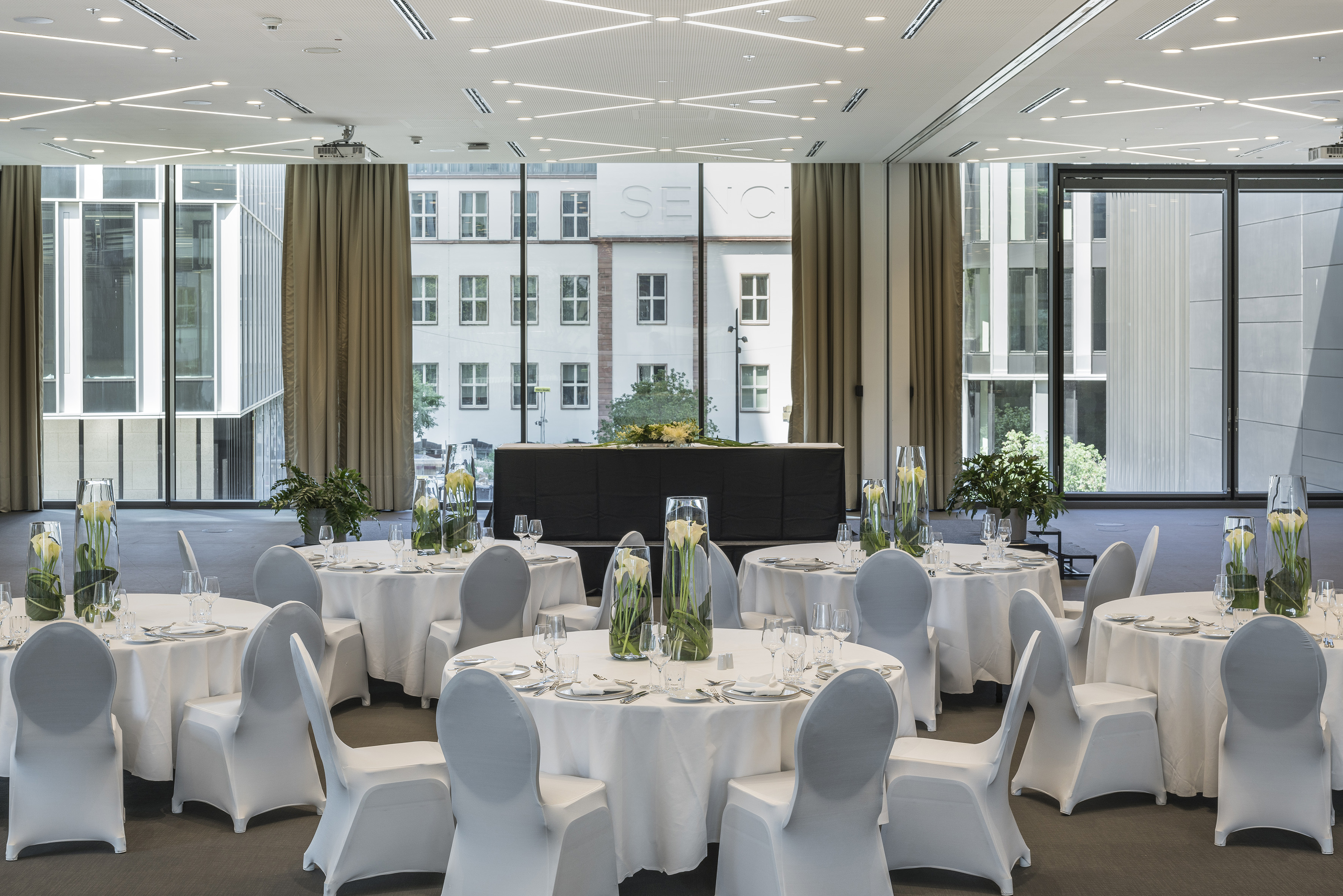 Elegant conference room with white banquet tables, calla lilies, city views.