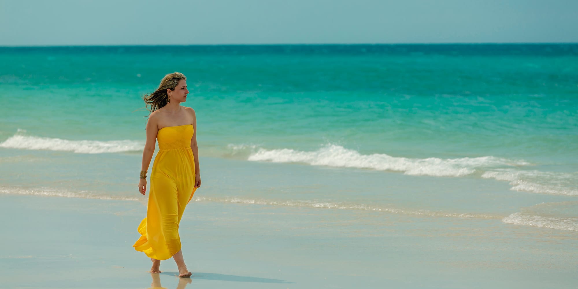 a woman in a yellow dress walking on a beach
