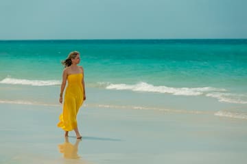 a woman in a yellow dress walking on a beach
