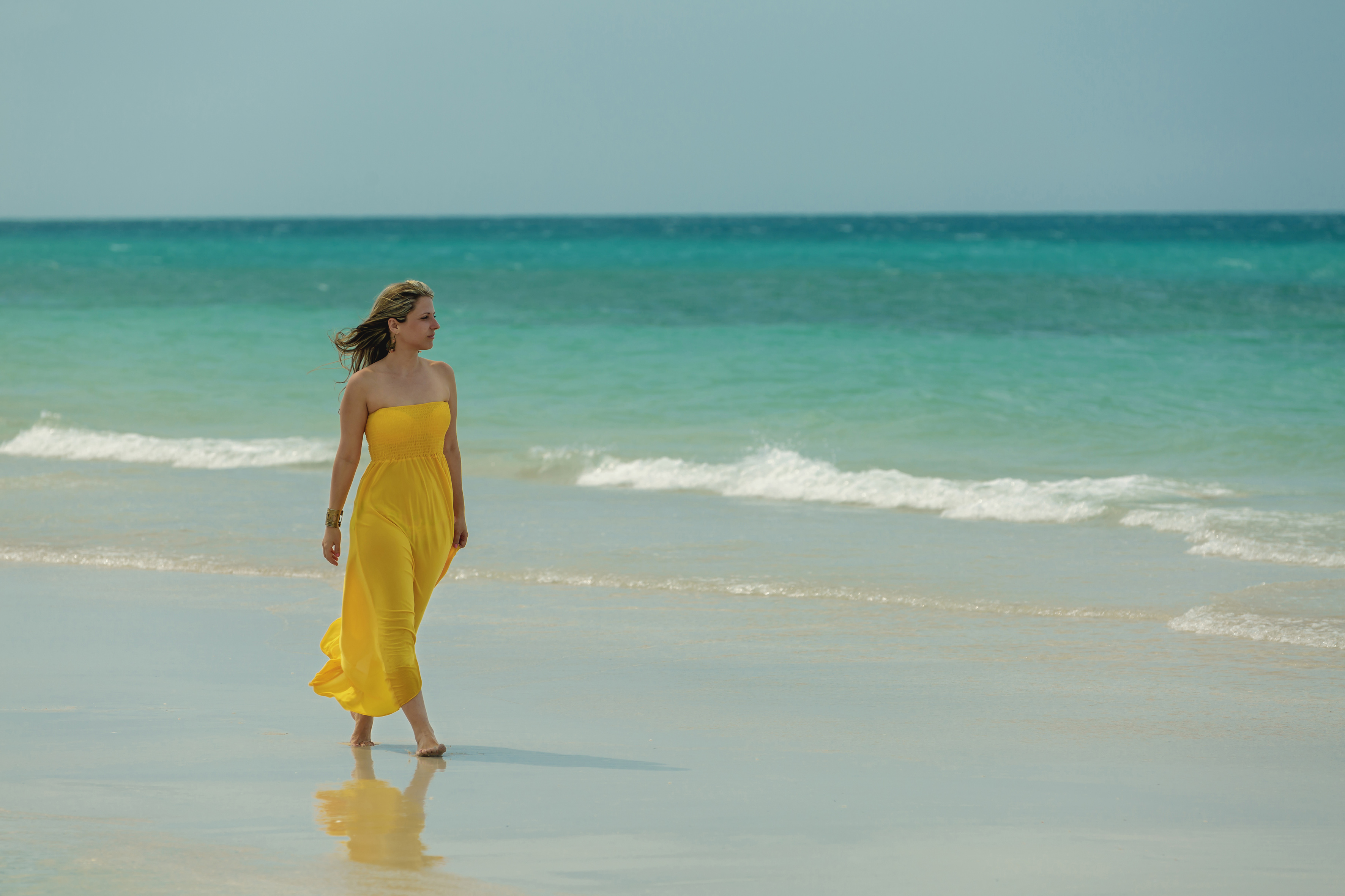 a woman in a yellow dress walking on a beach