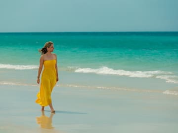 a woman in a yellow dress walking on a beach