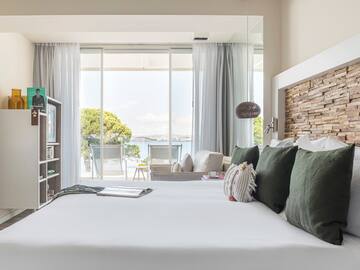 a bed with pillows and a bookcase in a room with a view of the water