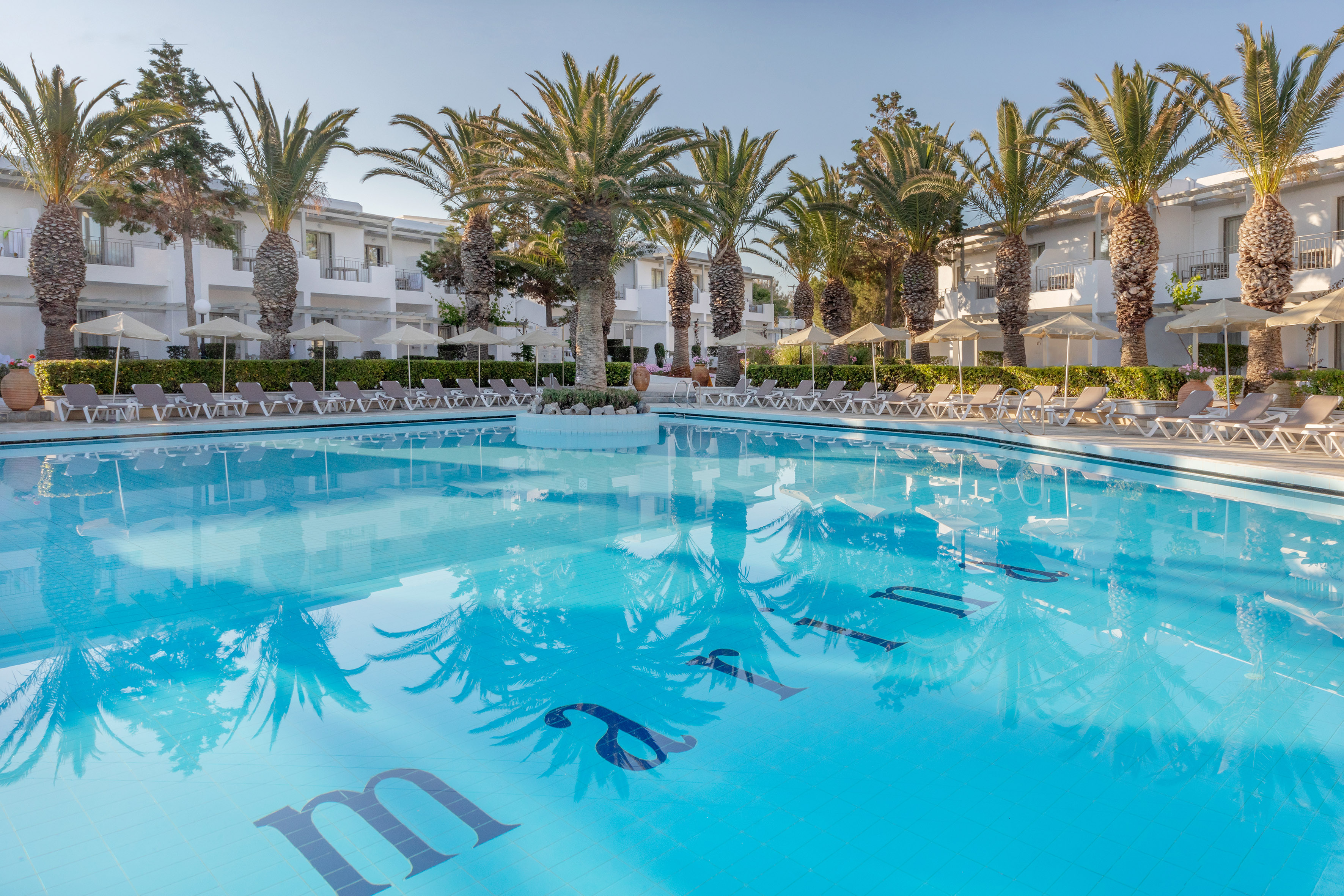 Sunny resort pool, palm trees, white hotel buildings, sun loungers.