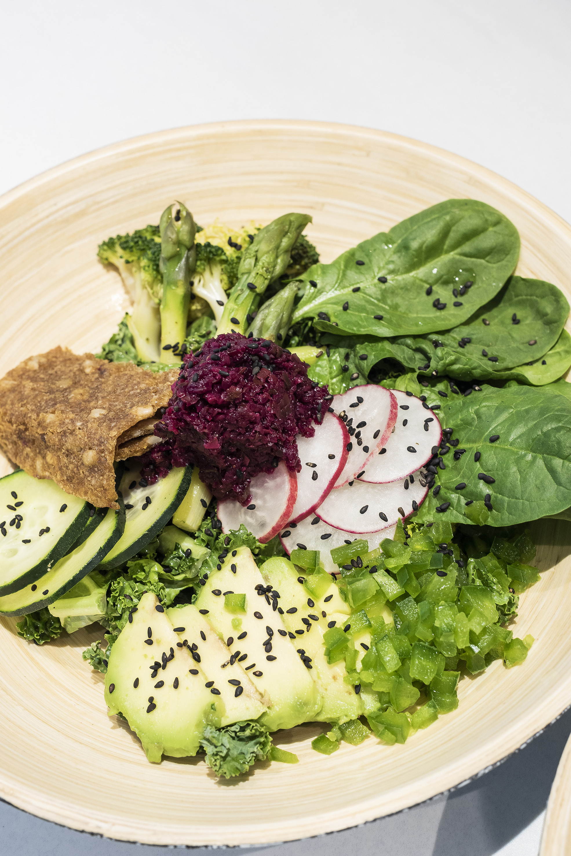 Vibrant vegan Buddha bowl: avocado, spinach, broccoli, radishes, beet spread.