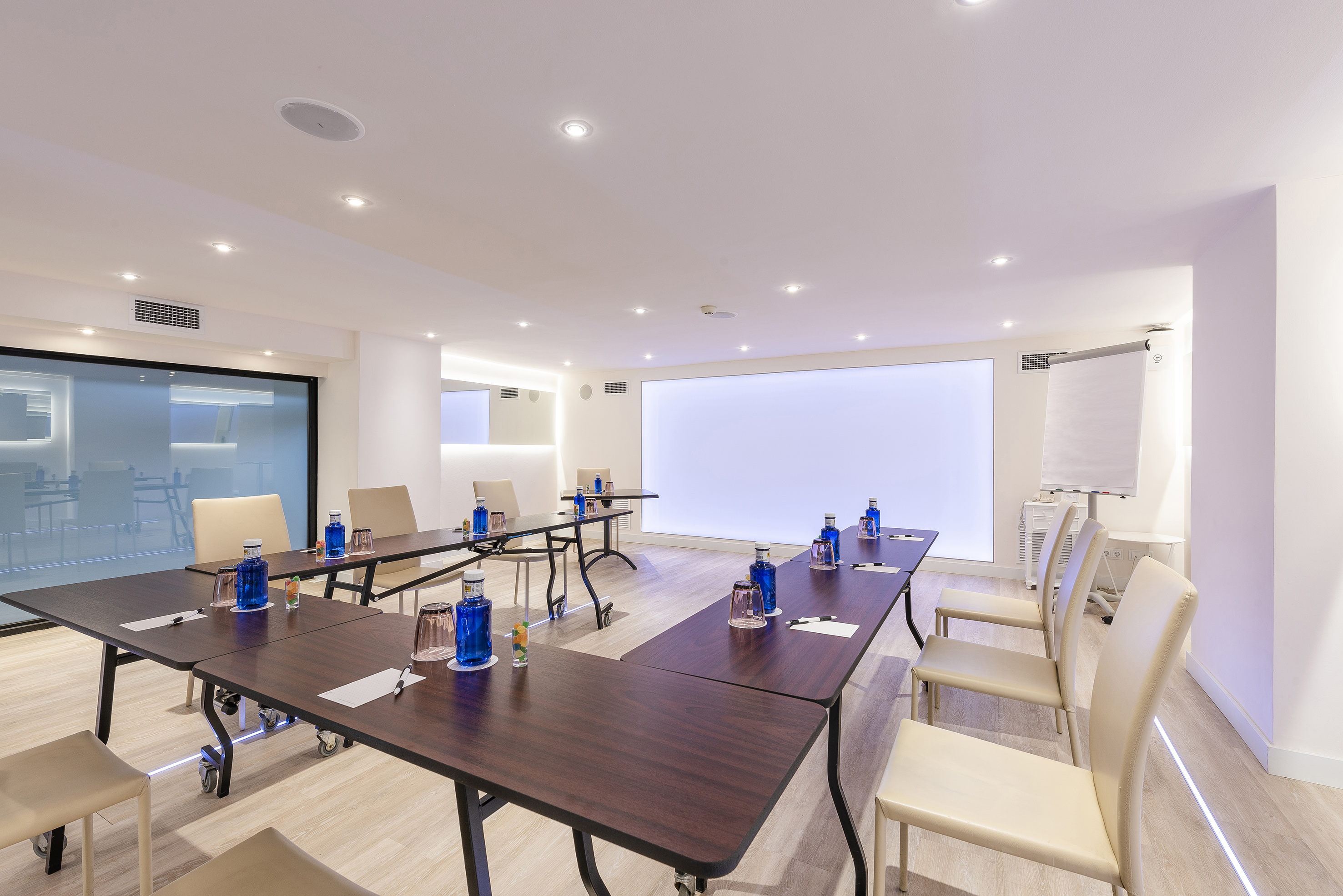 Modern meeting room with U-shaped table, large screen, and flipchart.