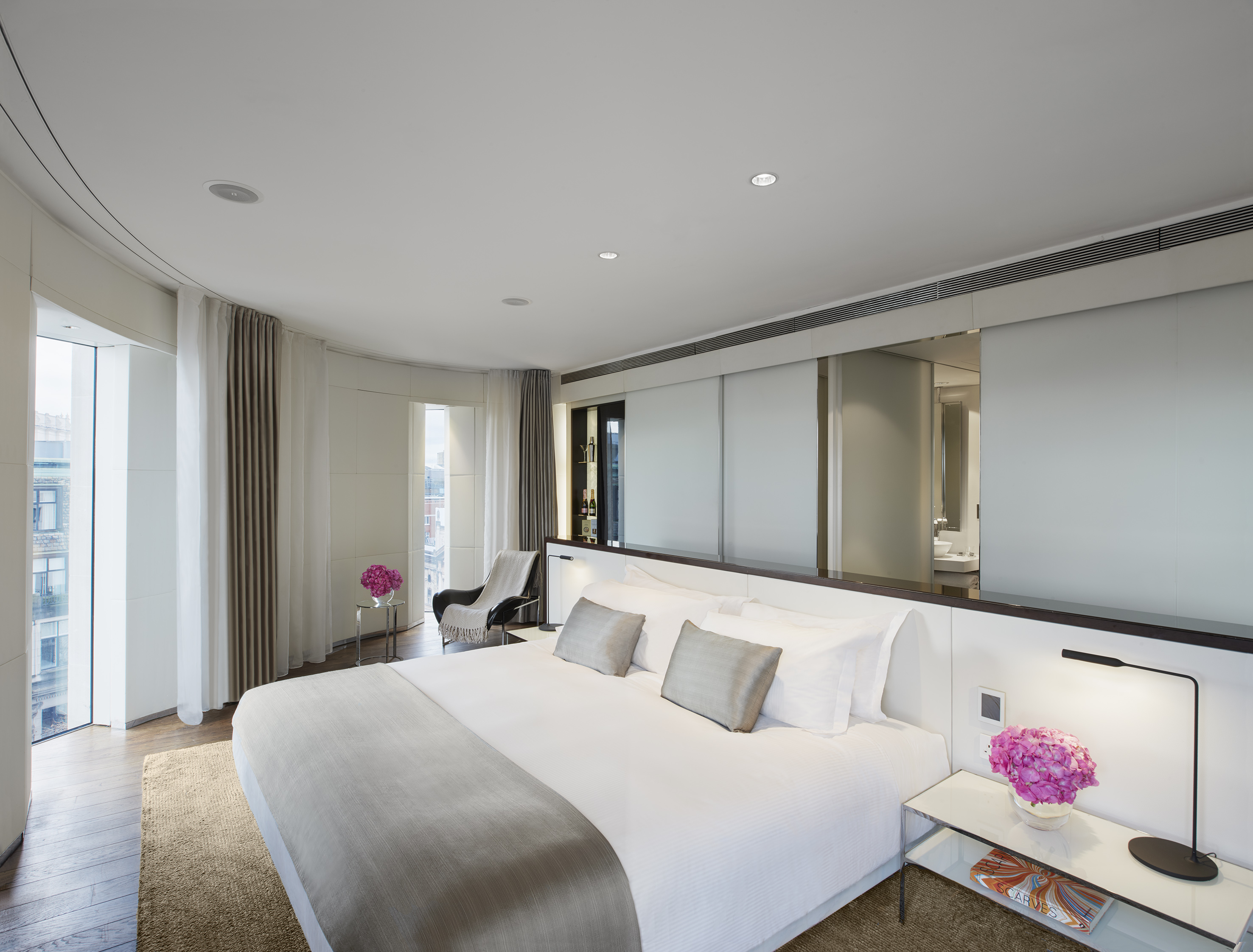 Luxury modern bedroom with king bed, curved windows, and sleek decor.